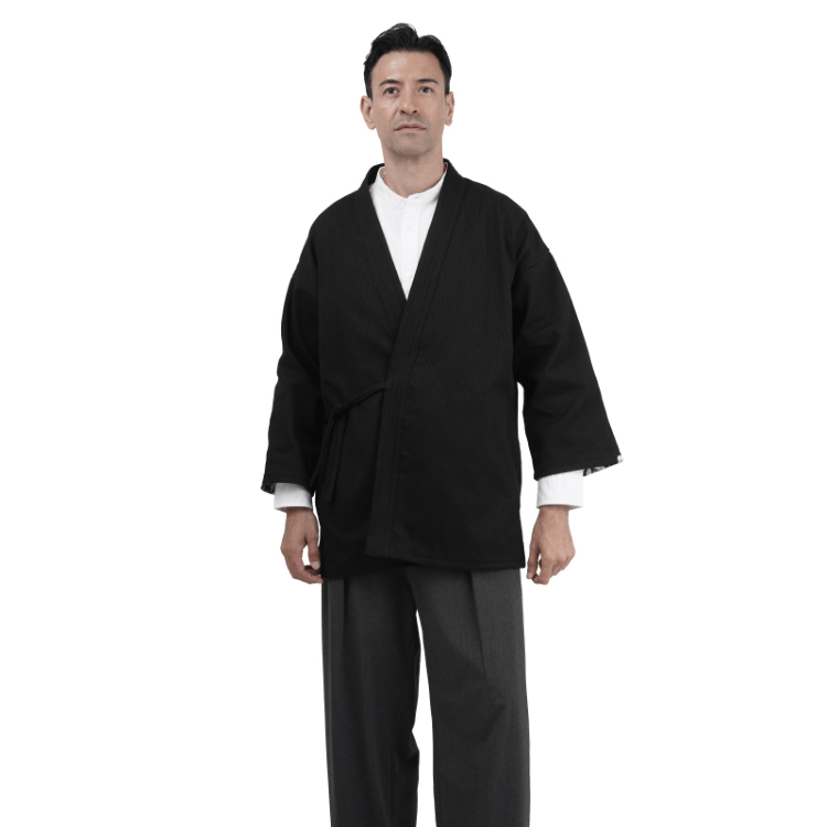 Man wearing a black martial arts Sashiko Judo Gi jacket and gray pants, standing with arms relaxed at sides against a plain white background.
