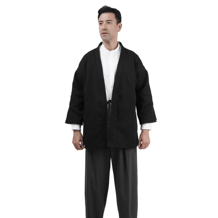 Man wearing a black martial arts Sashiko Judo Gi jacket over a white shirt and gray pants.