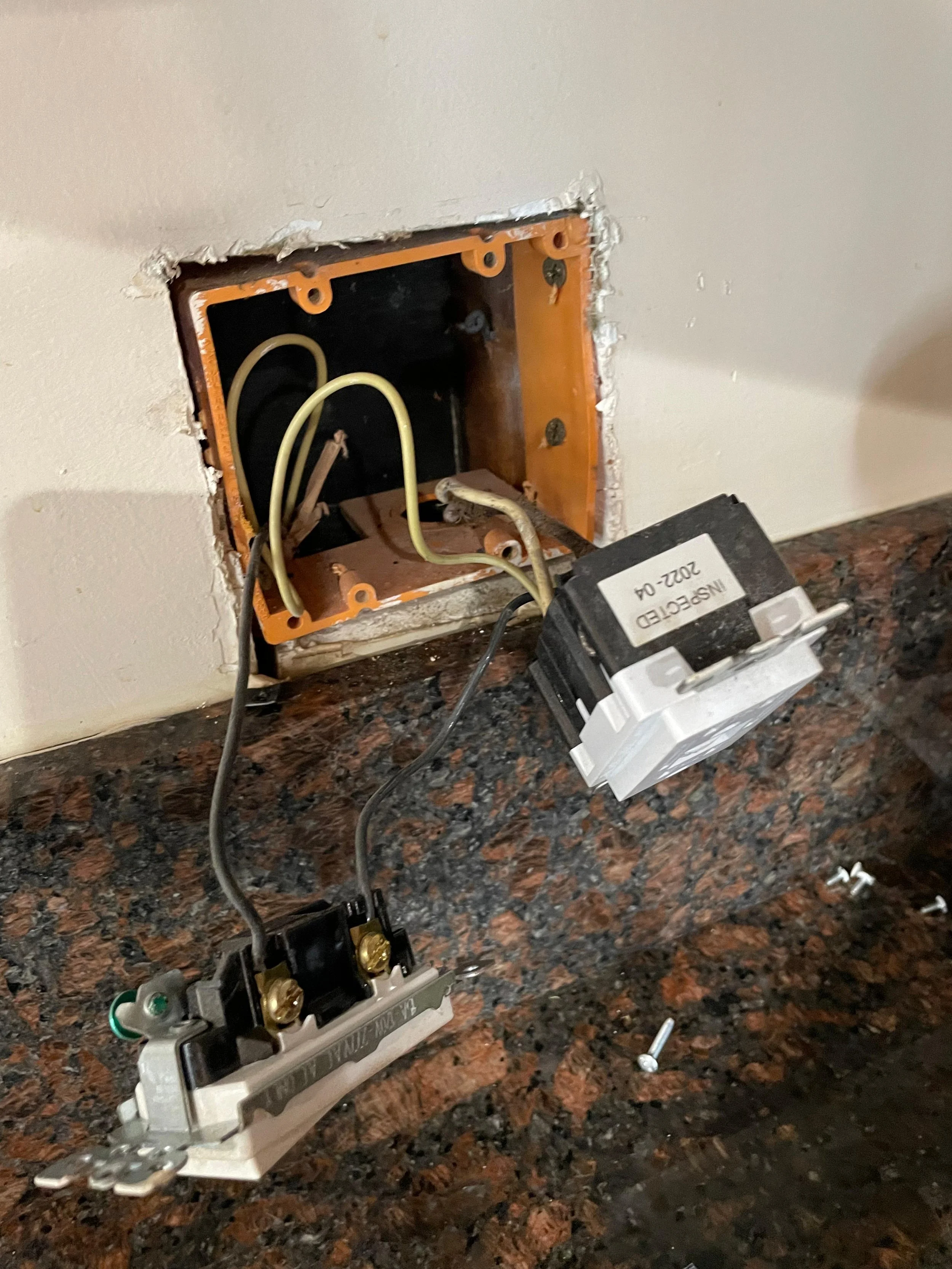 Open electrical box with wires, a power outlet, and a circuit breaker on a kitchen countertop.