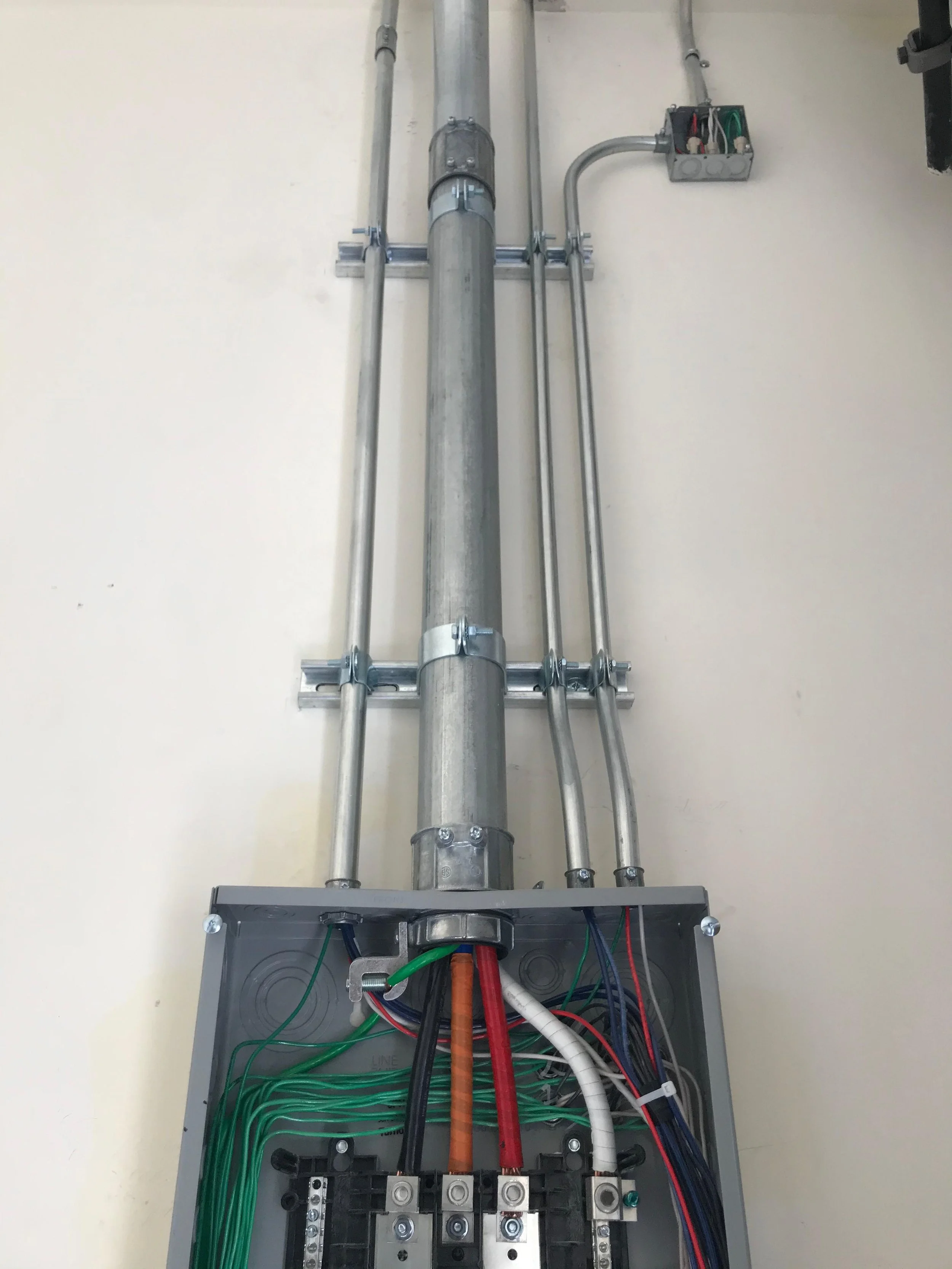 Electrical junction box with multiple colored wires connected and metallic conduit pipes.