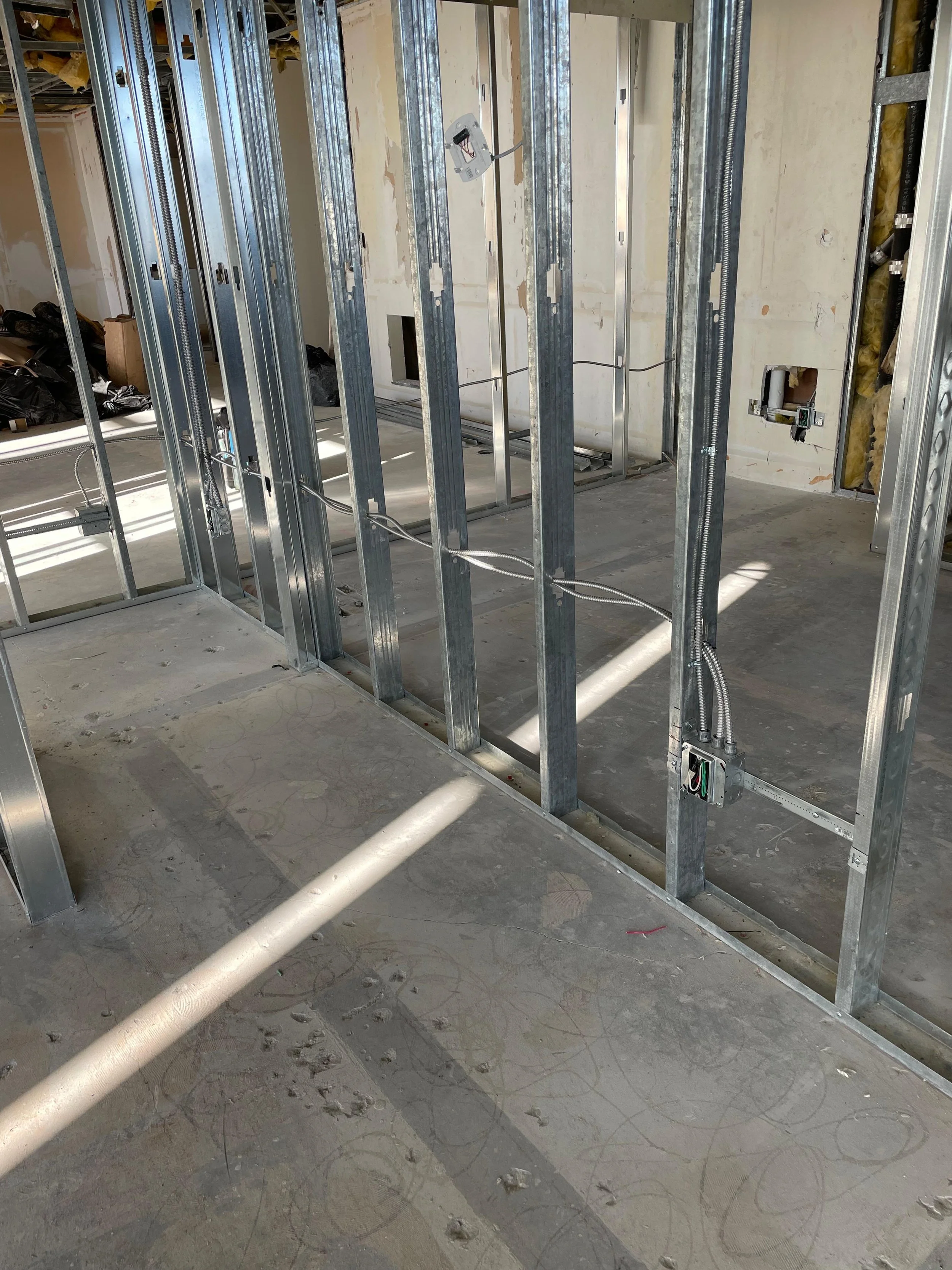 Interior view of a building under construction with metal framing, electrical wiring, and a concrete floor.