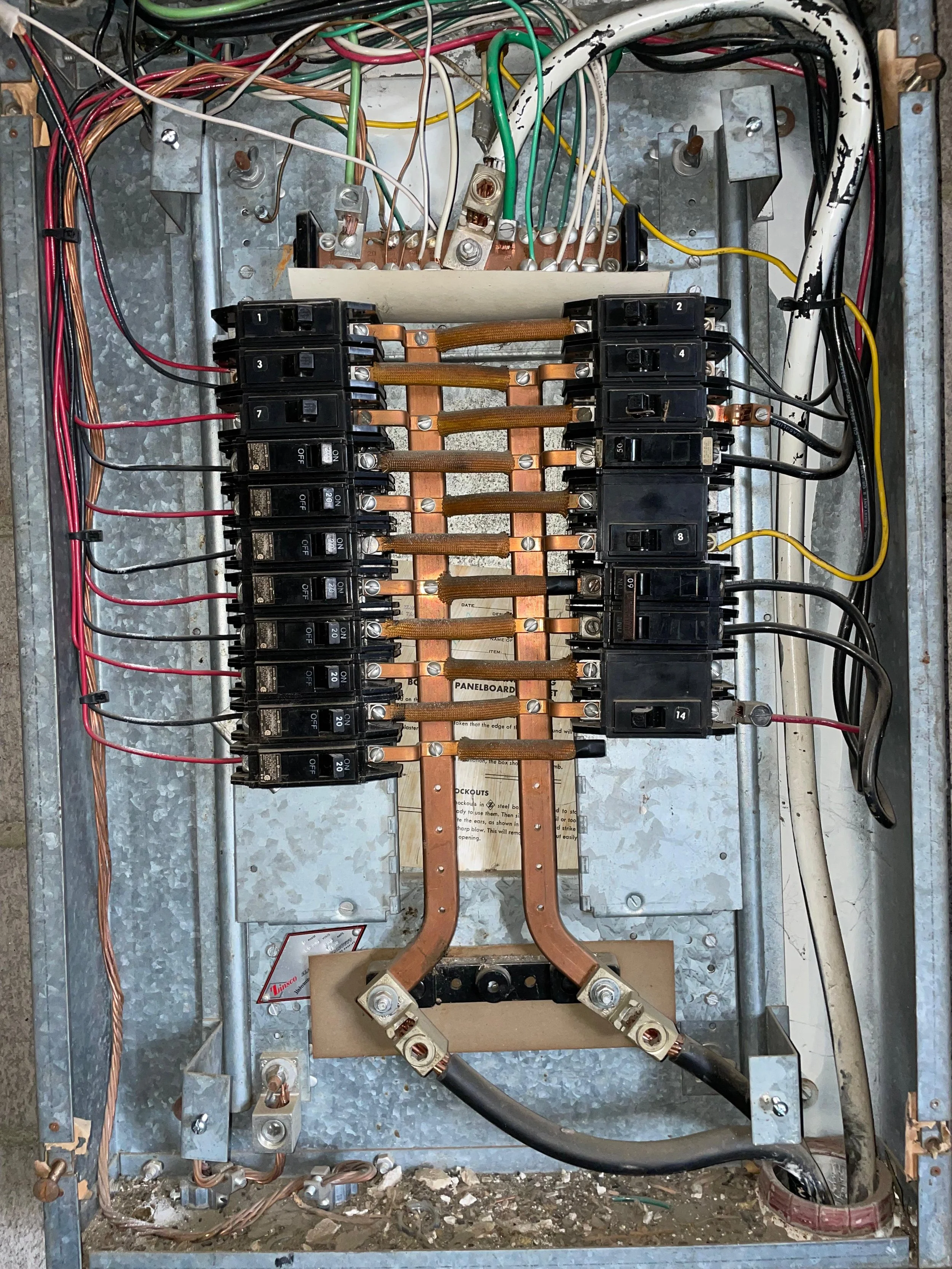 Electrical panel with circuit breakers, copper wiring, and grounding cables inside a metal enclosure.