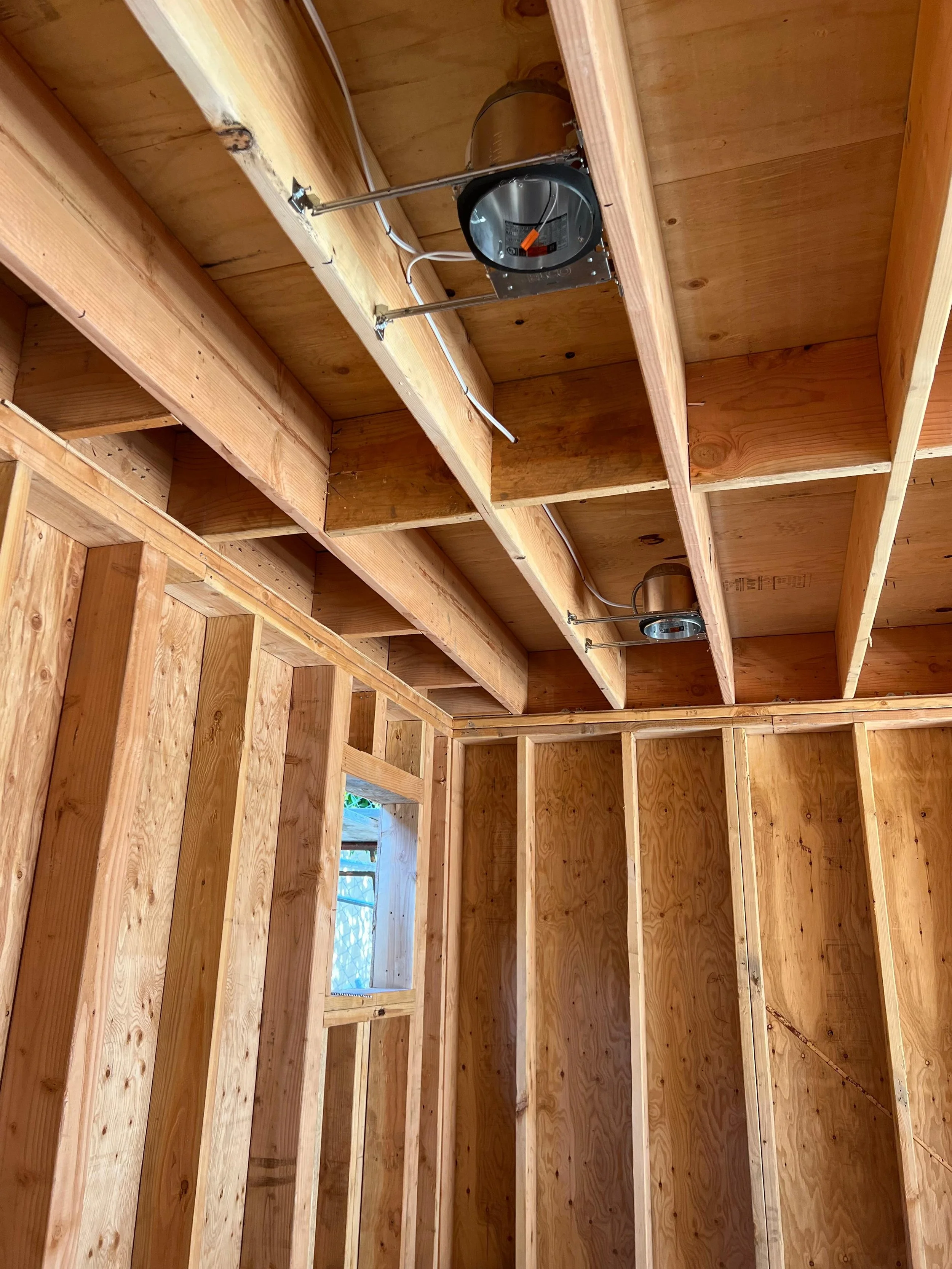 Interior of a wooden framed structure under construction, with visible beams and two light fixtures mounted to the ceiling.