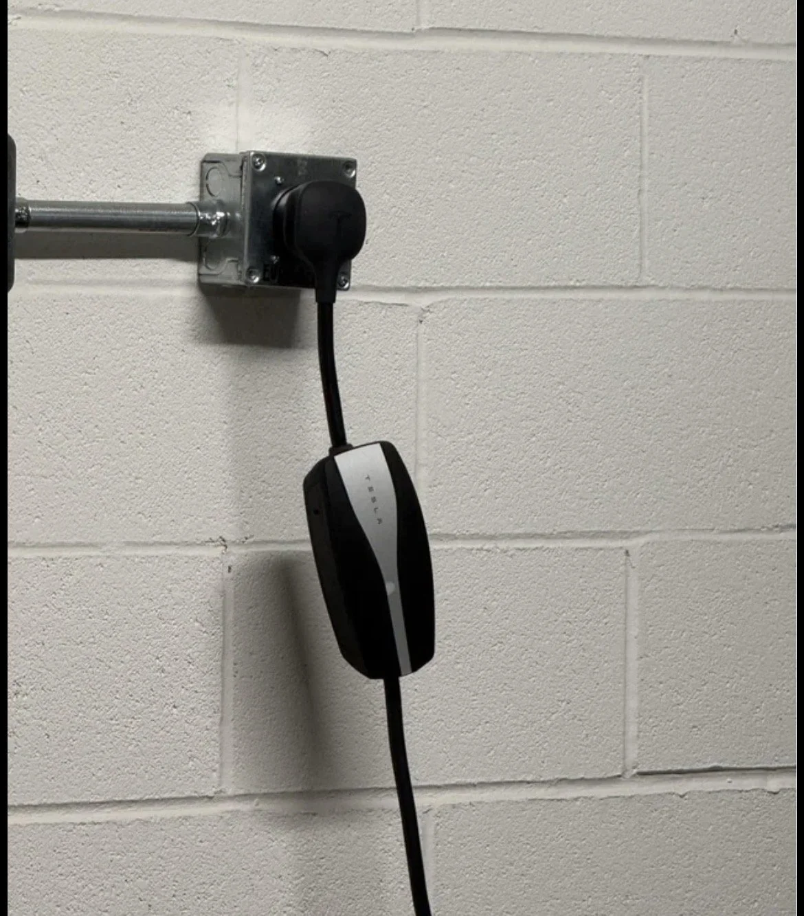 Electrical outlet on a white brick wall with a black device plugged into it.