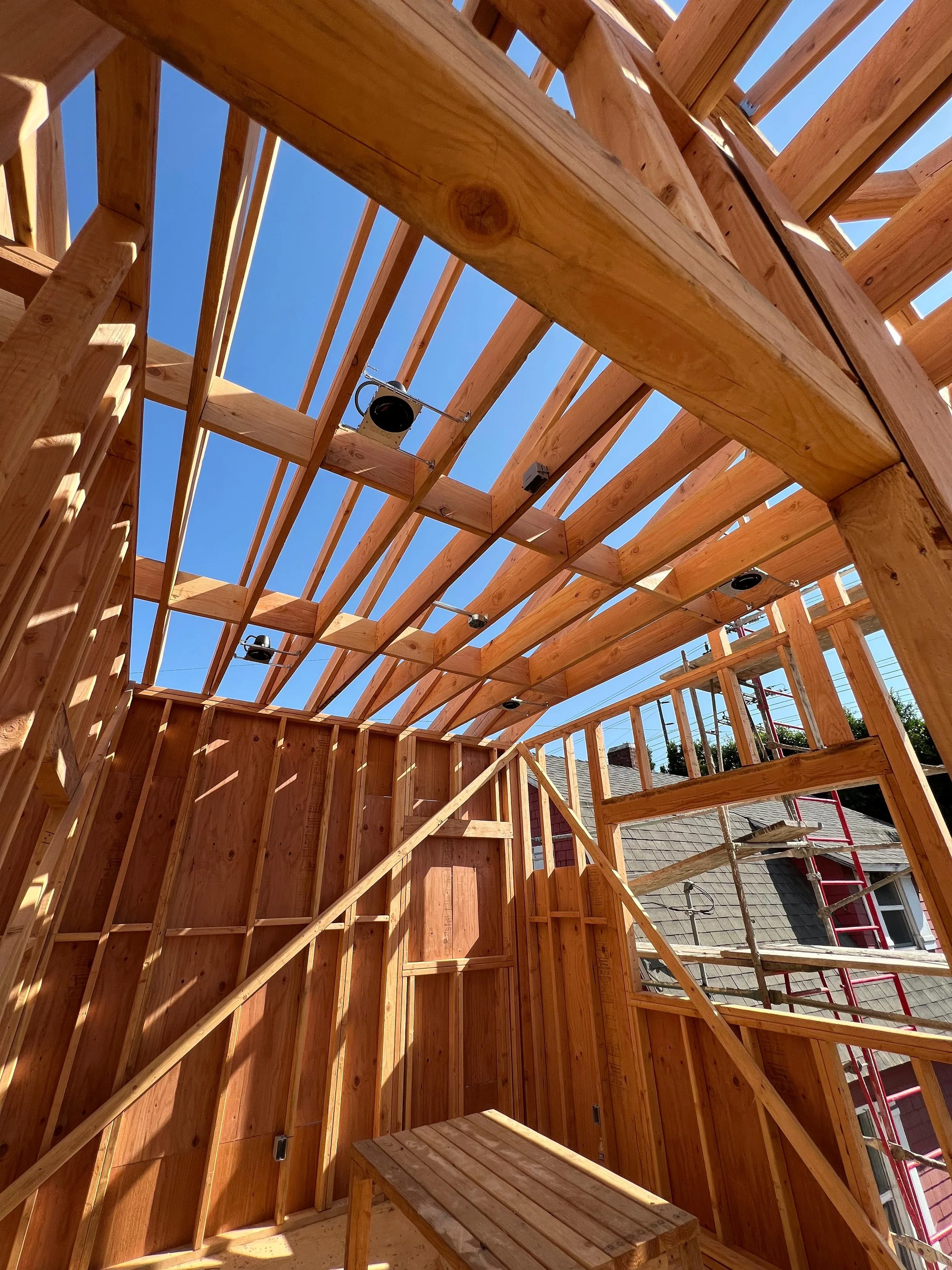 Wooden framing of a building under construction with scaffolding and a clear blue sky visible through the roof openings.