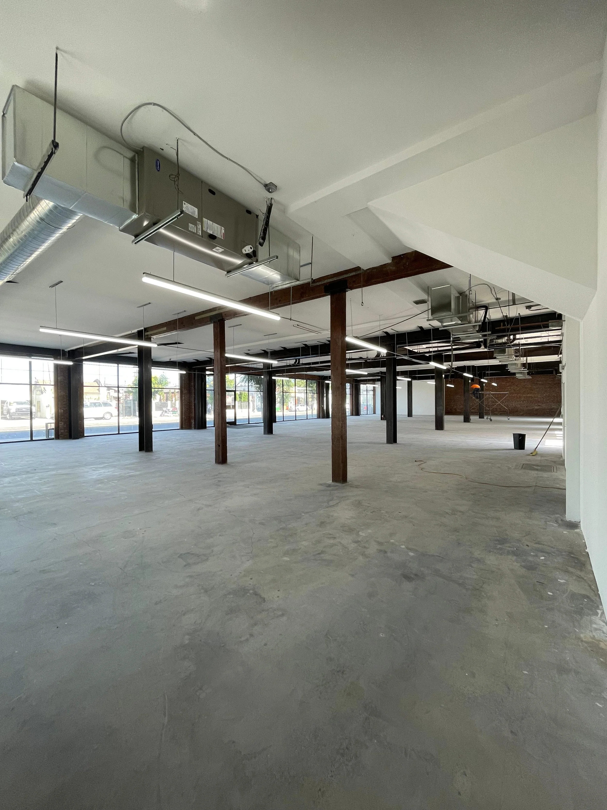 An unfinished commercial or office space with exposed HVAC ducts, wooden support beams, large windows, and a concrete floor.