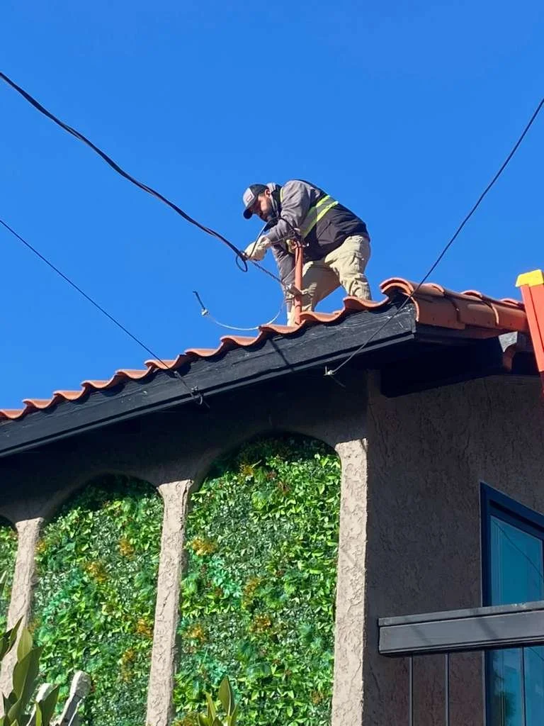 A worker in safety gear on a roof working on a wire cable outside a house with landscaped green wall panels.