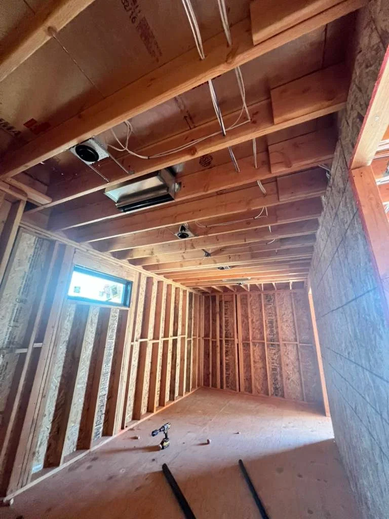 Interior of a building under construction with exposed wooden framing, electrical wiring, and a small window.