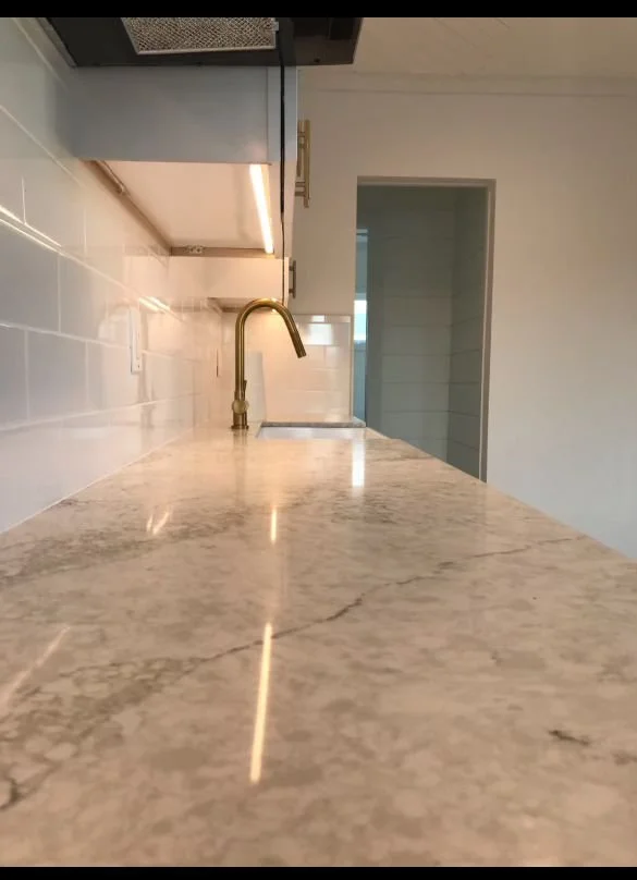 Close-up view of a kitchen countertop with a marble surface, gold faucet, and white tile backsplash.