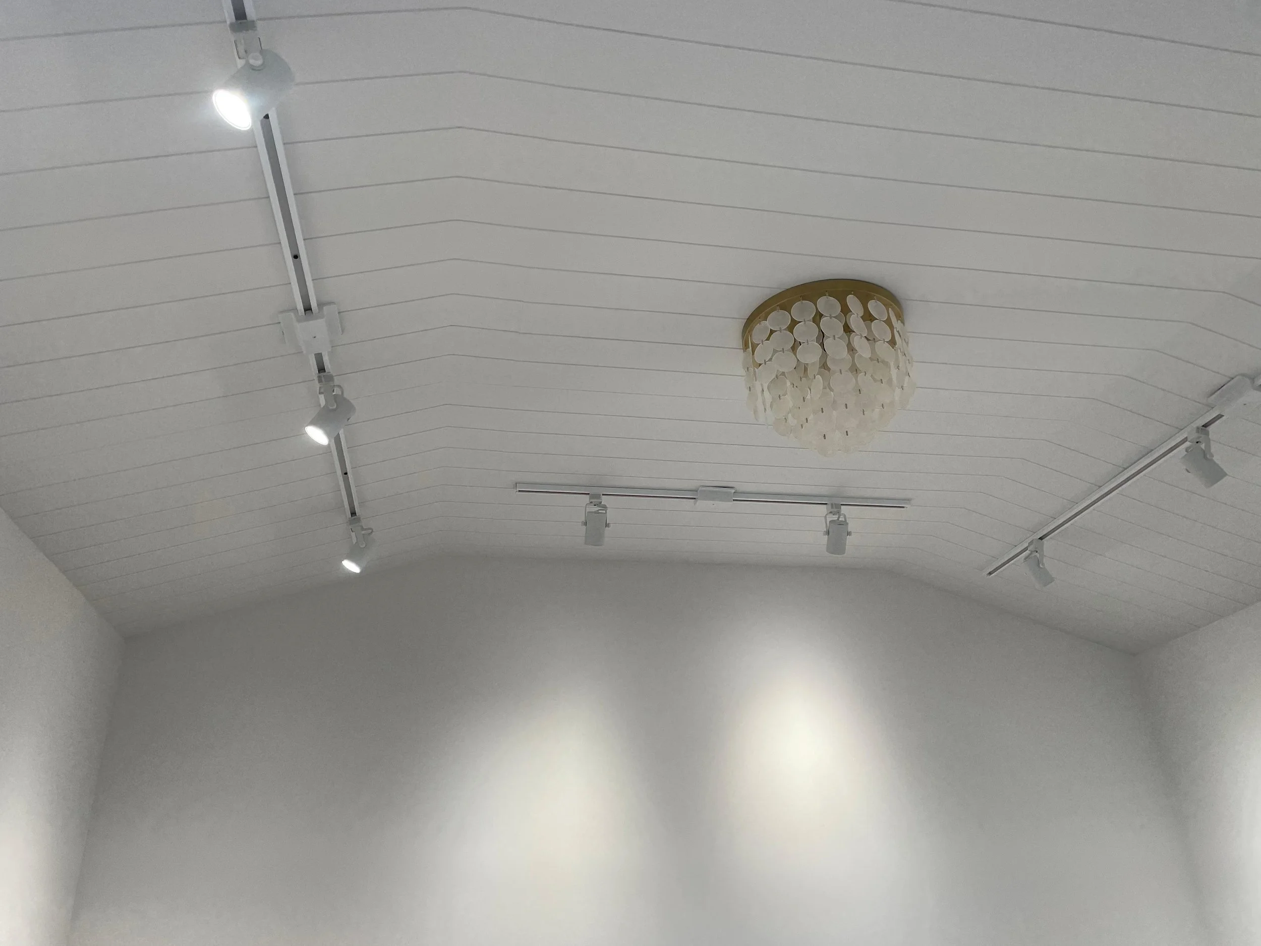 Ceiling with track lighting and a decorative chandelier in a white room.