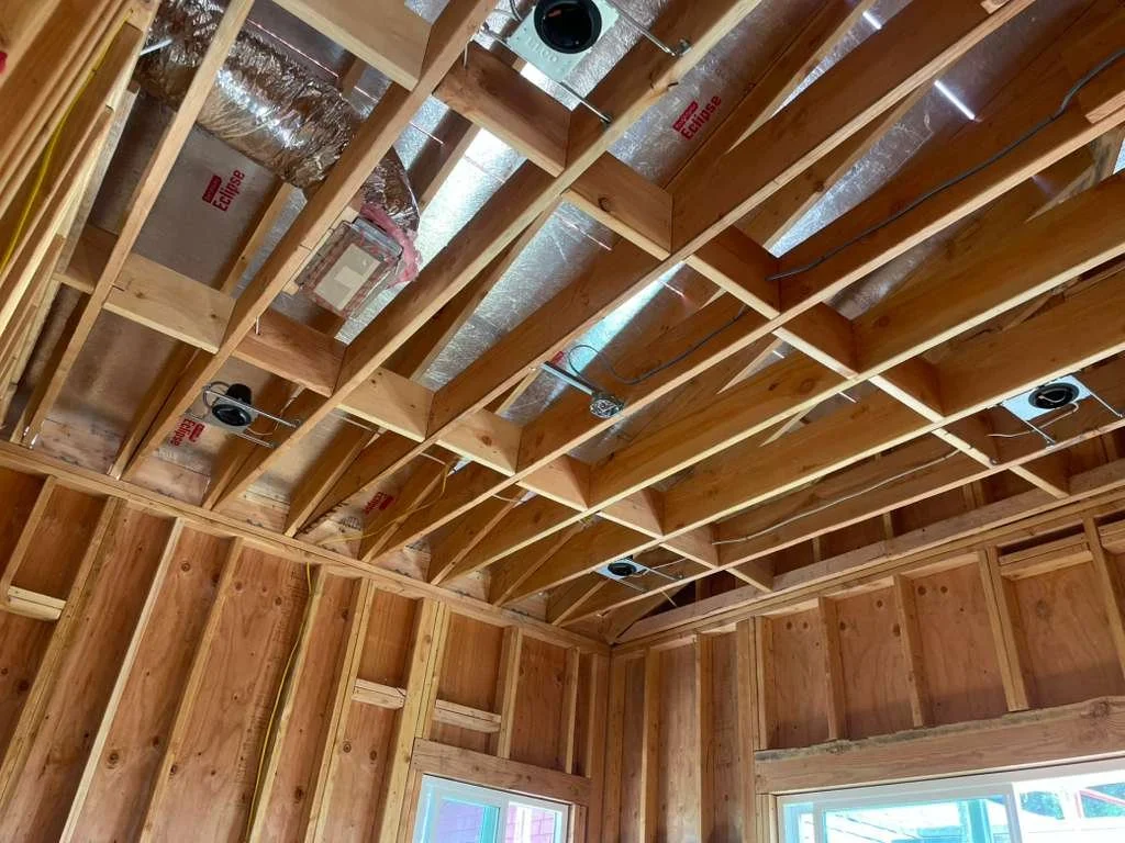 View of a framed ceiling space with exposed wooden beams, wiring, and ductwork in a room under construction.