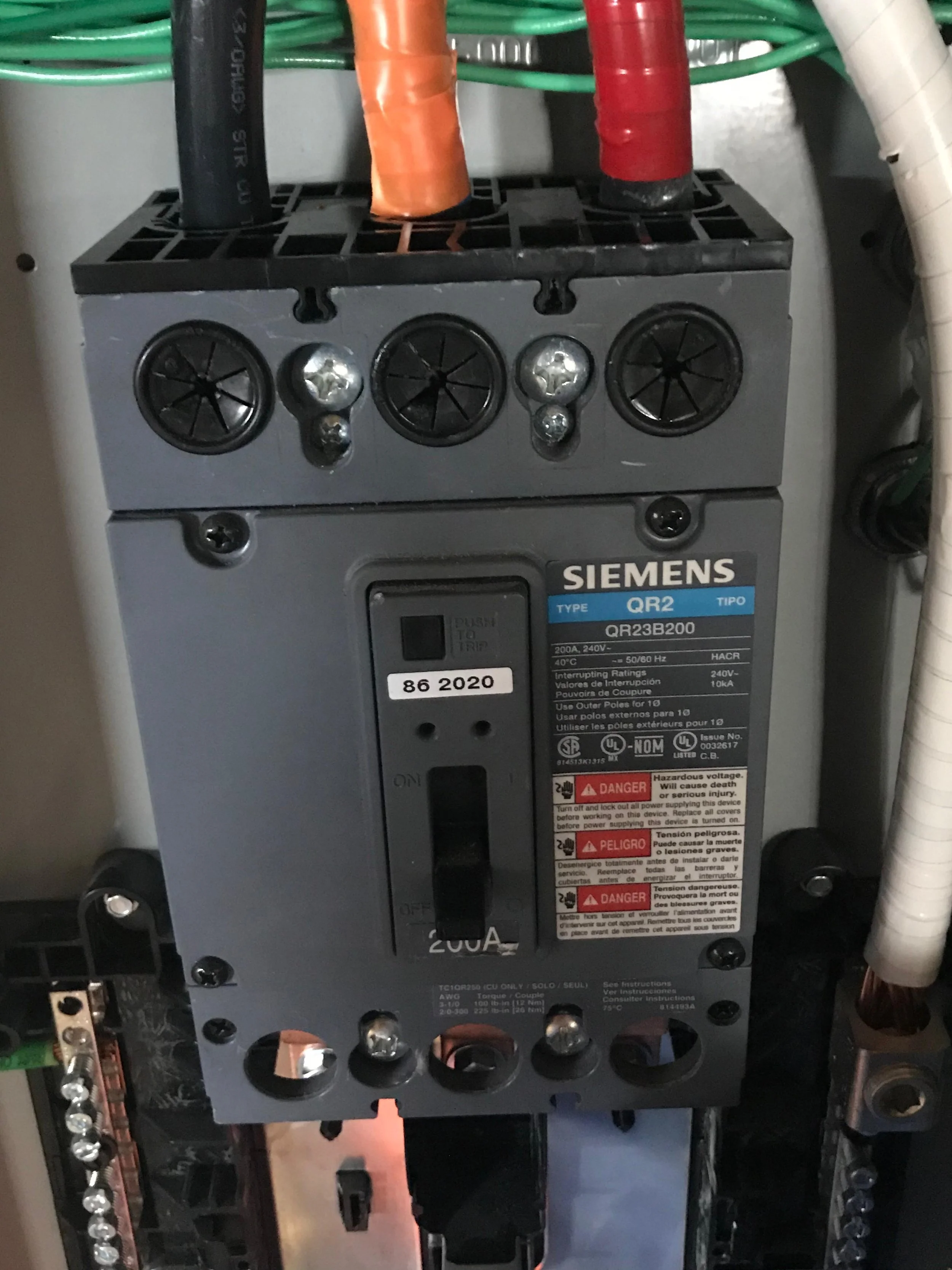 Close-up photo of an industrial electrical motor or circuit breaker, labeled Siemens QR2 with warning labels, screws, and connection points visible.