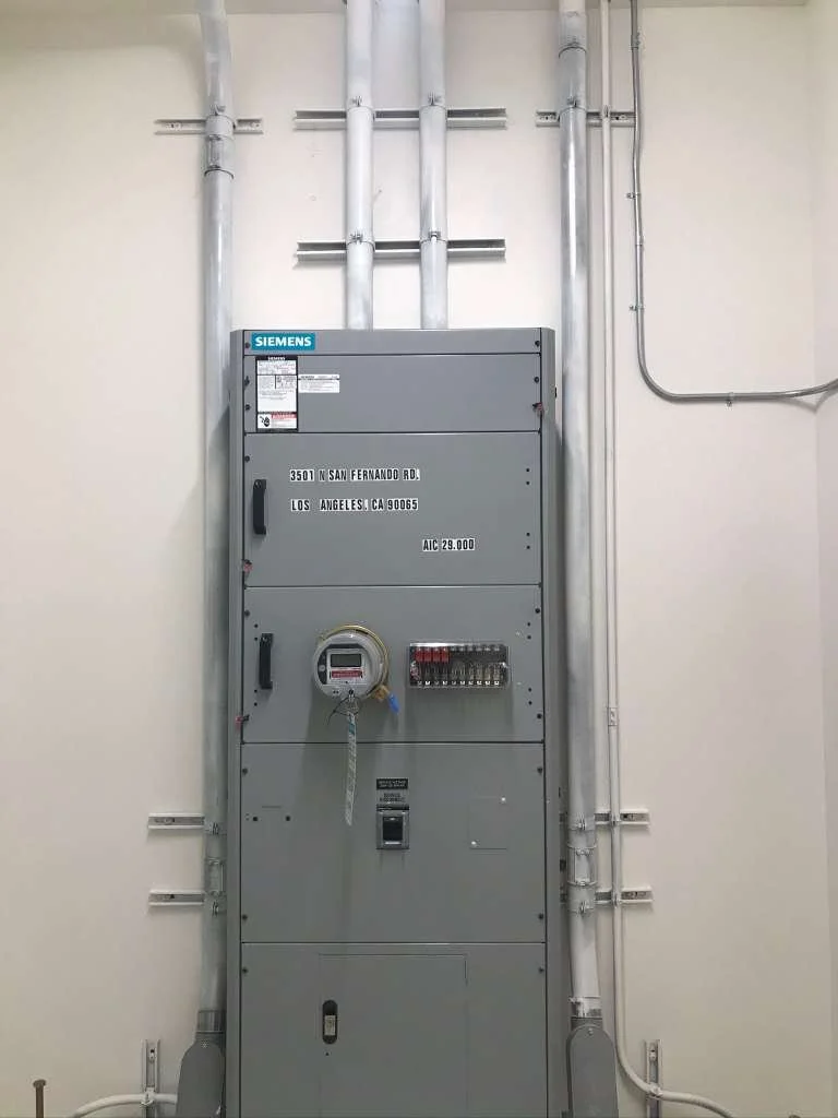 Electrical electrical panel with multiple pipes and conduits in a utility room.