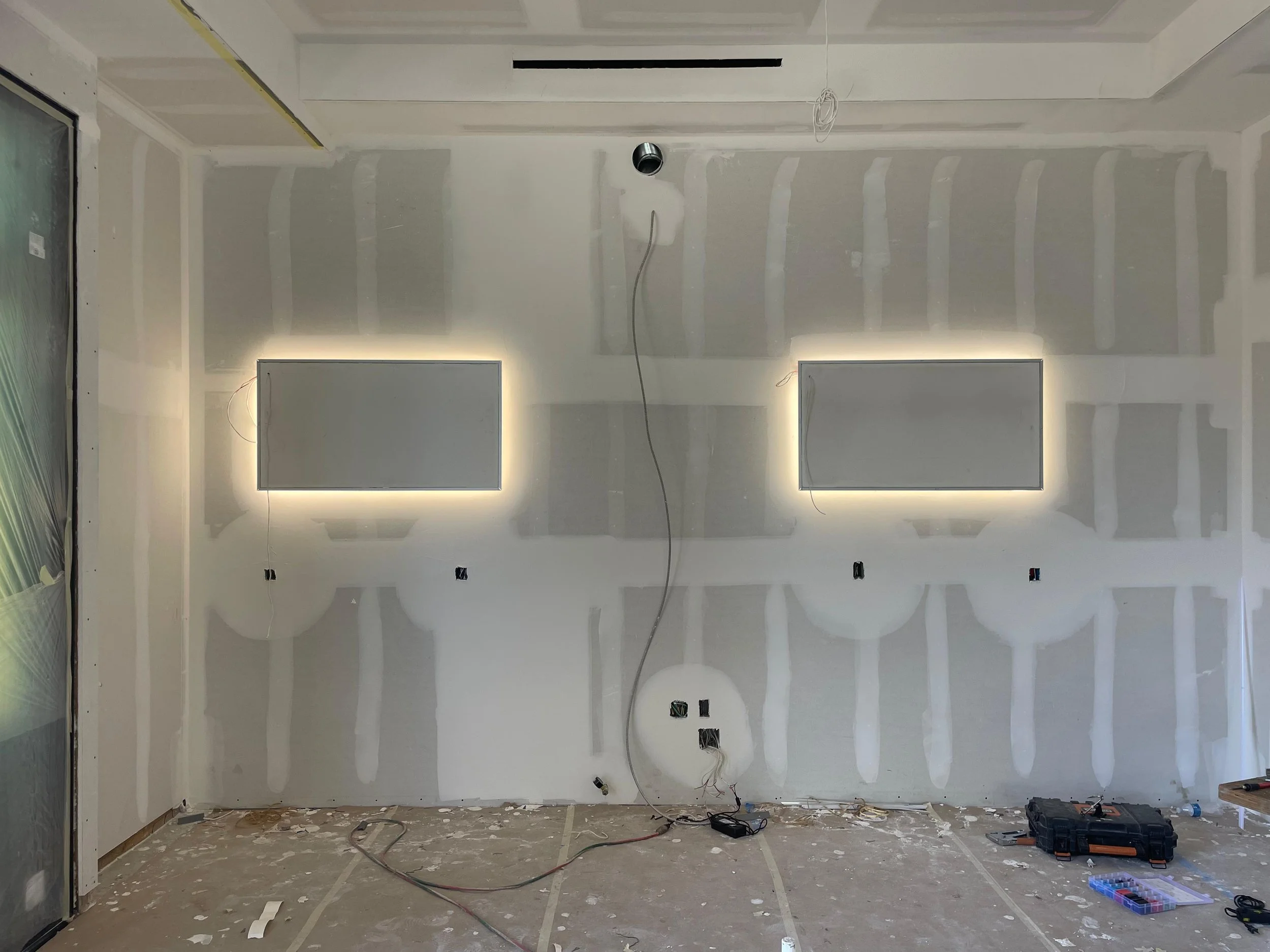 Unfinished room under construction with drywall installed, electrical wires hanging, and construction tools and debris on the floor.