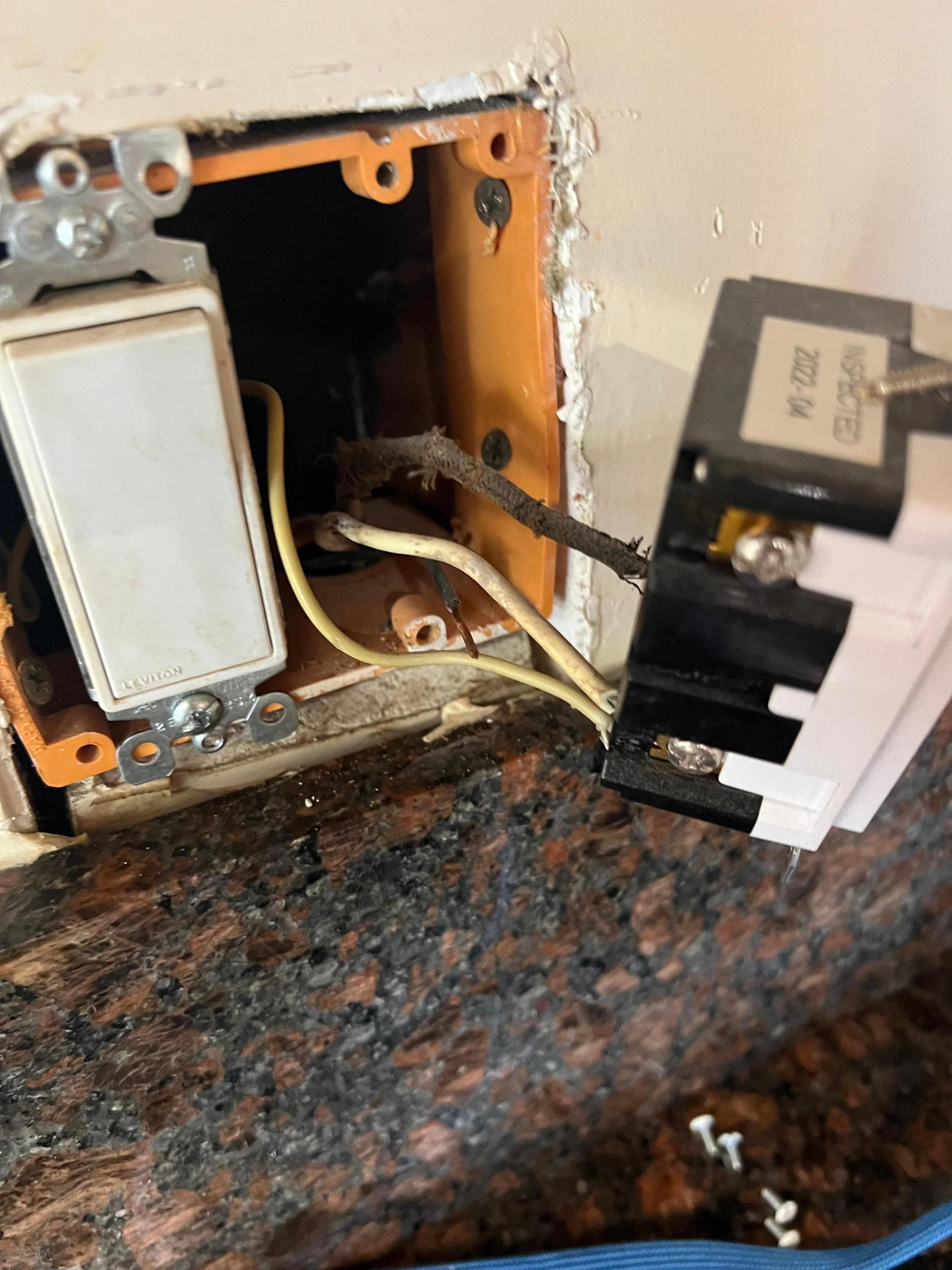 Close-up of the inside of an electrical or electronic device with wires, screws, and circuit components visible, sitting on a speckled dark and reddish-brown countertop.