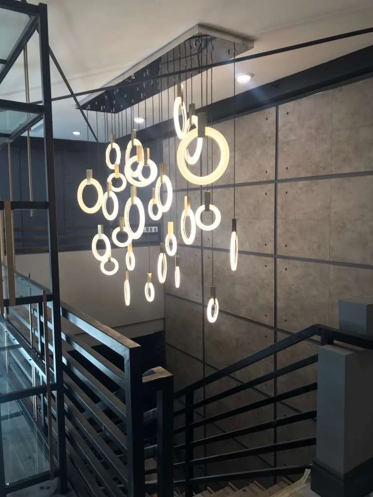 Modern staircase with hanging circular and ring-shaped pendant lights in a building interior.