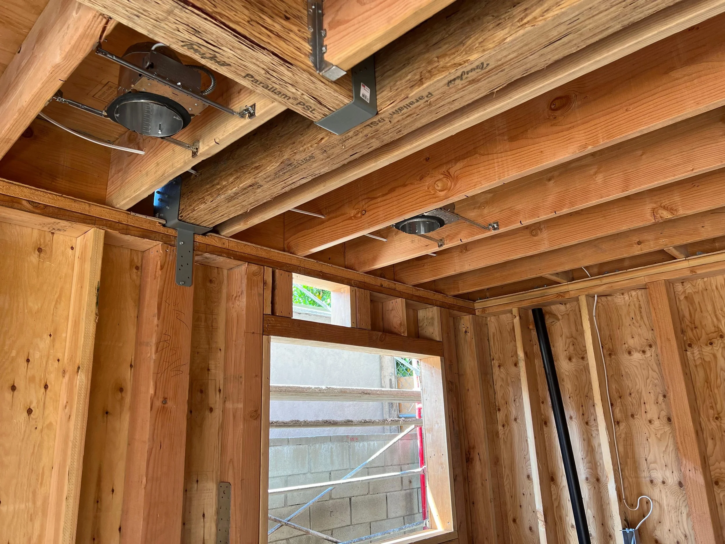 Interior view of a construction site showing wooden beams, metal framing brackets, HVAC ductwork, and wires installed in the ceiling.