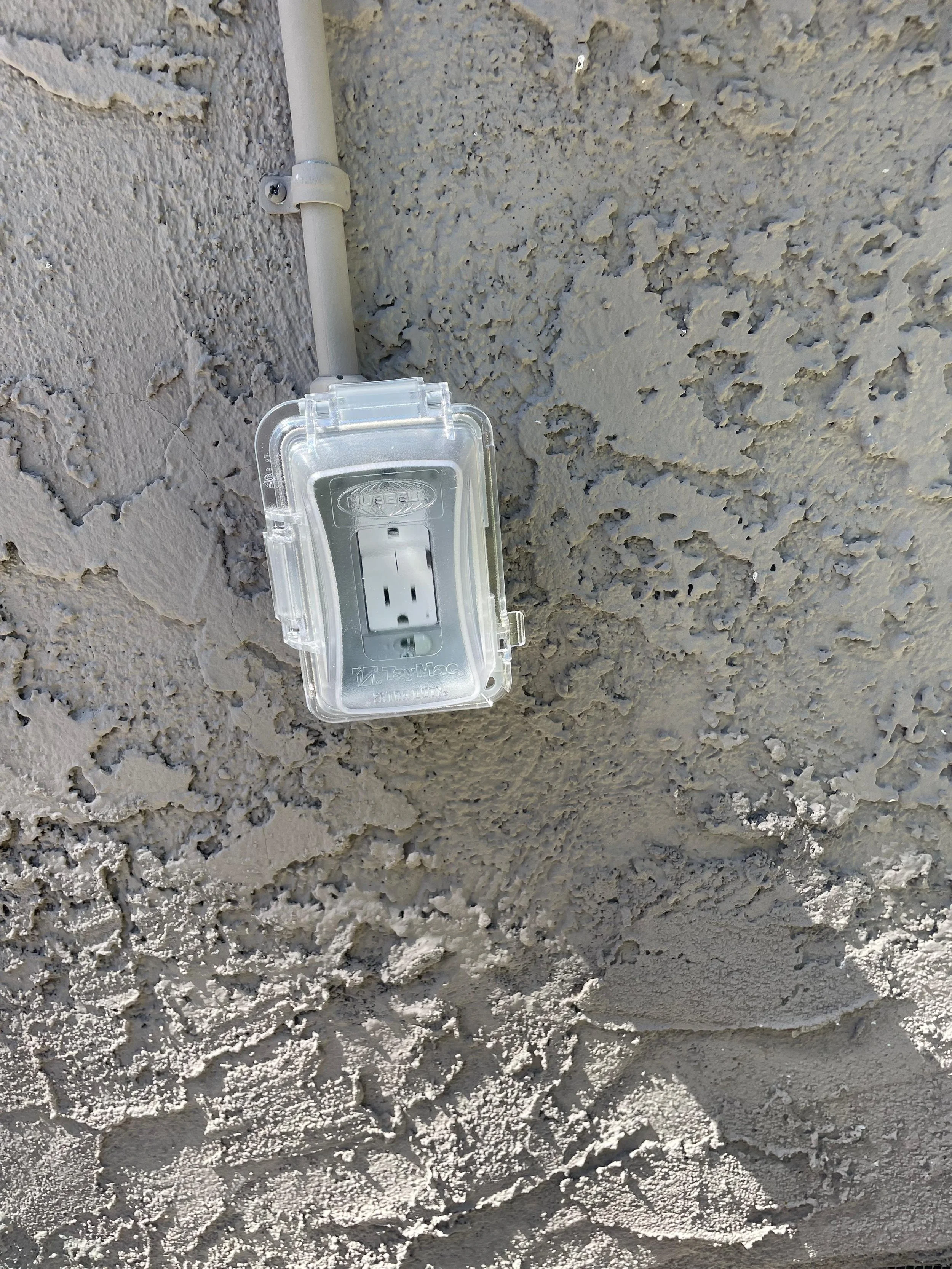 A plastic electrical outlet cover with a power socket attached to a textured beige exterior wall.