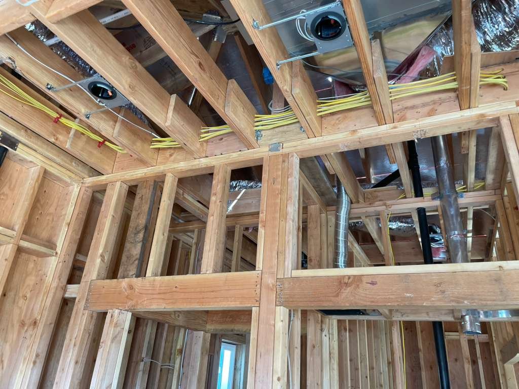 Interior view of a building under construction, showing wooden framing, electrical wiring, and HVAC ducts.