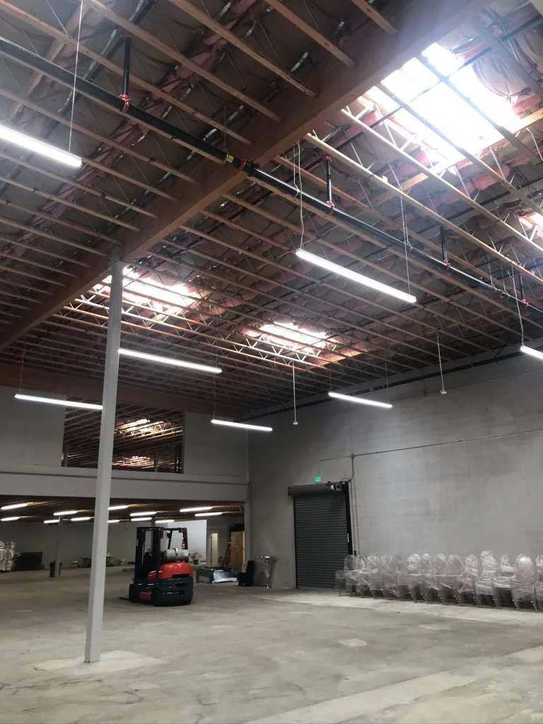 Empty warehouse with exposed ceiling, fluorescent lights, a forklift, and stacked plastic containers.