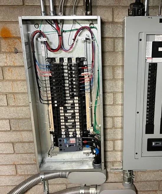 Open electrical breaker box with wiring connected inside, mounted on a brick wall.