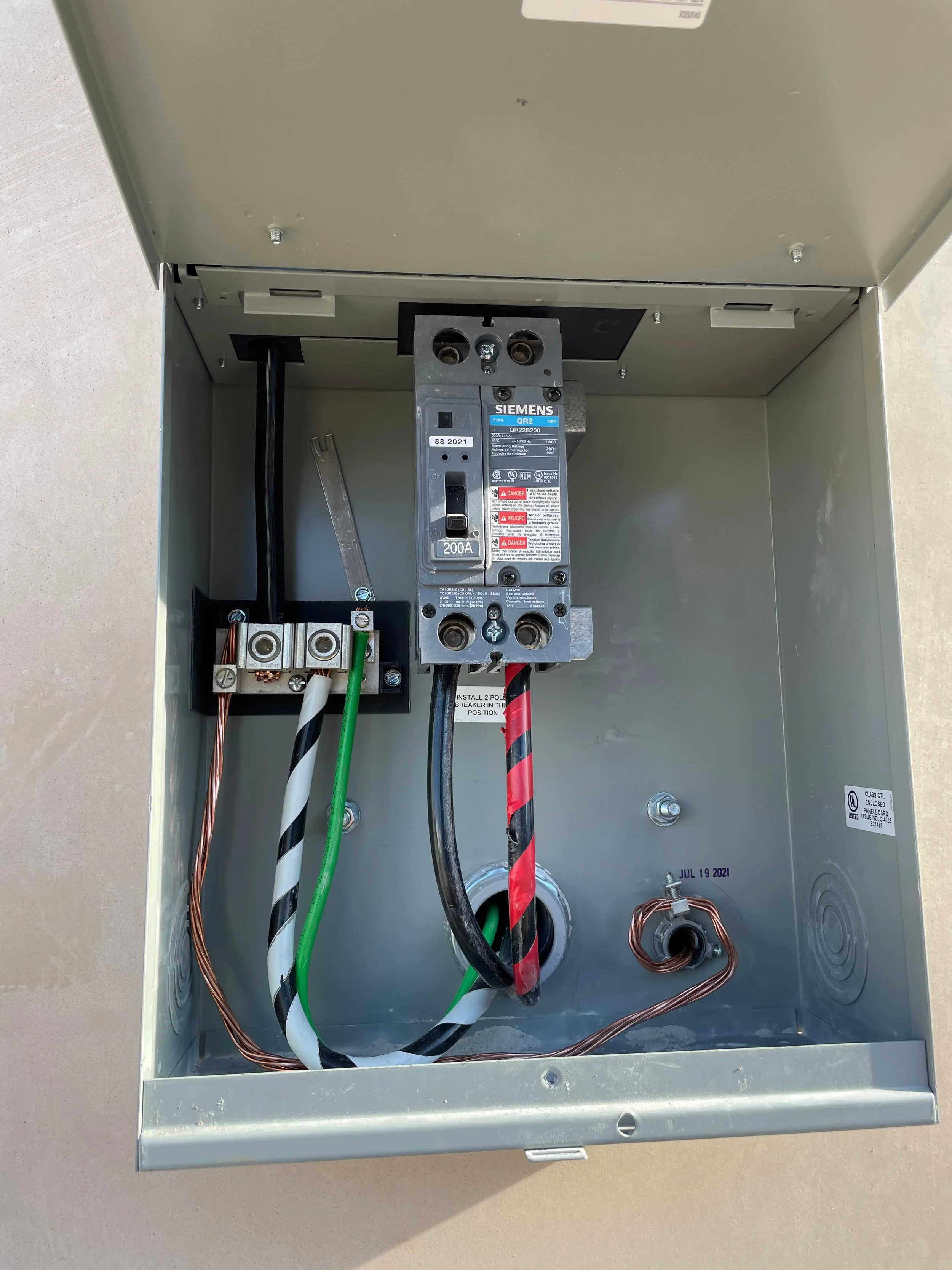 Open metal electrical box with wiring and a circuit breaker inside.