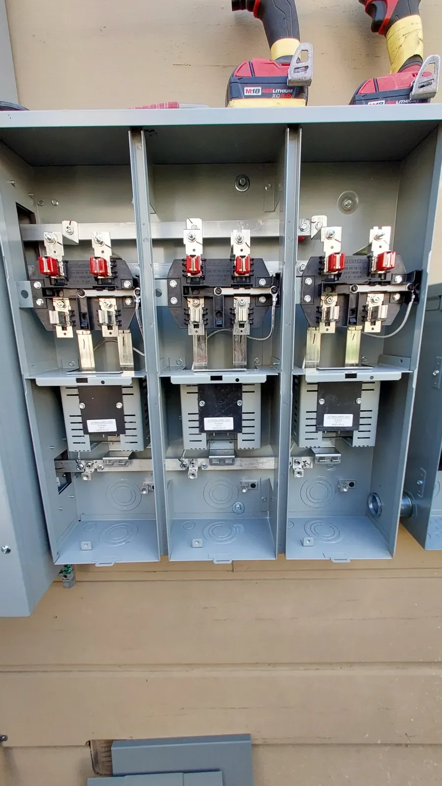 Open electrical panel with three circuit breakers and electrical wiring, placed on a wooden surface.