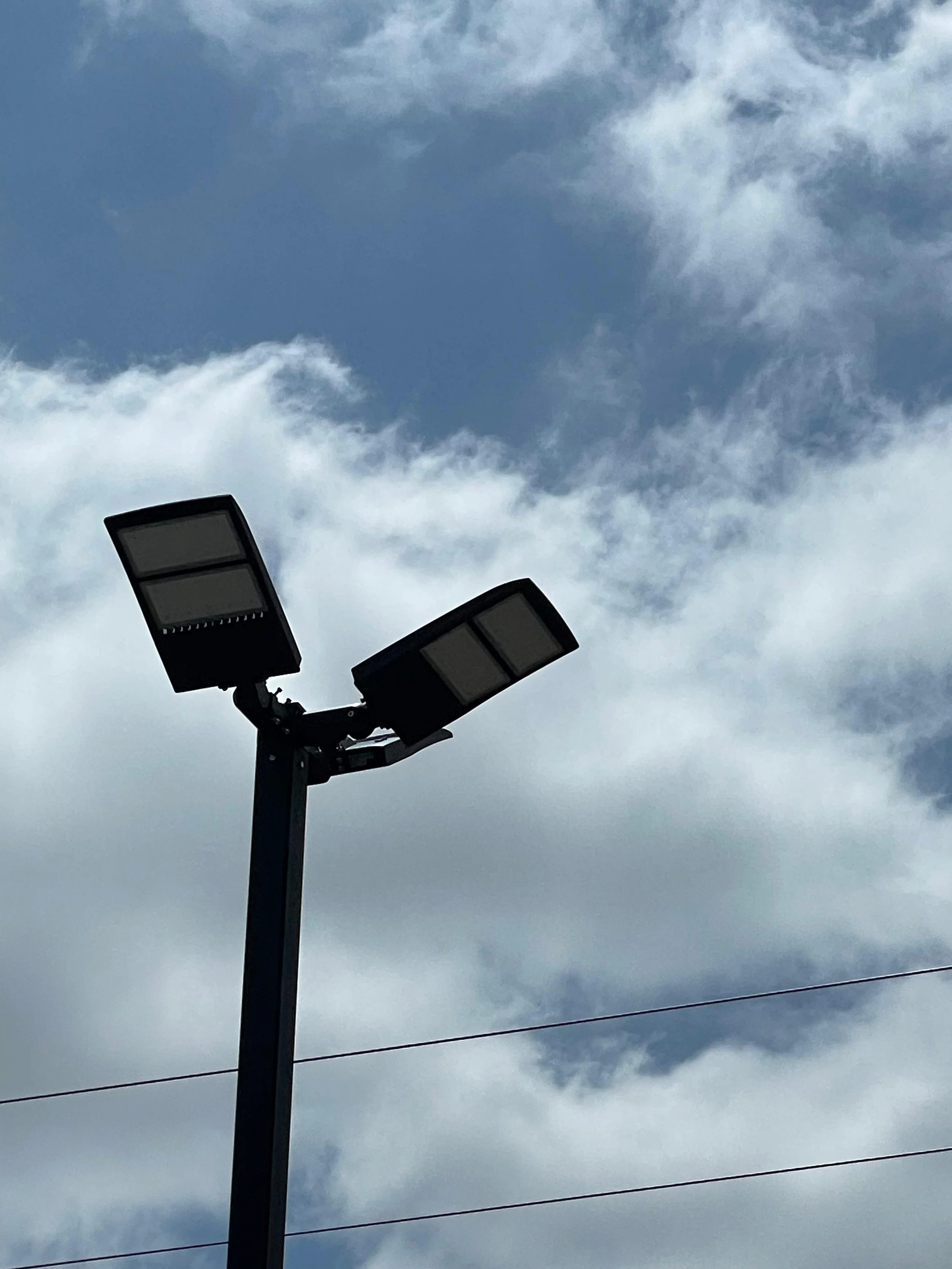 Streetlight with two rectangular LED panels against a cloudy sky.