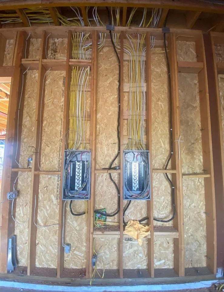 Electrical wiring and panels installed in a building wall, with exposed wooden studs.