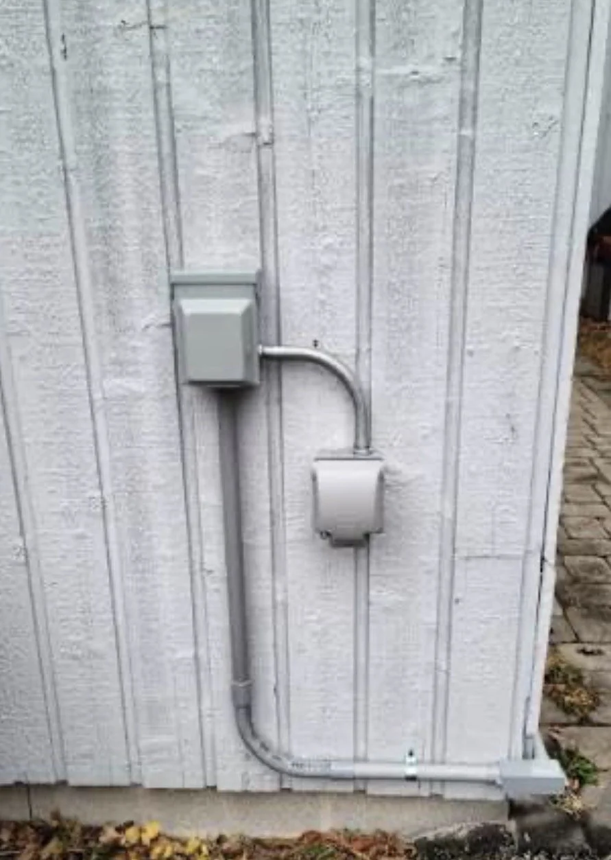 Electrical box and conduit attached to a white wooden wall outside.