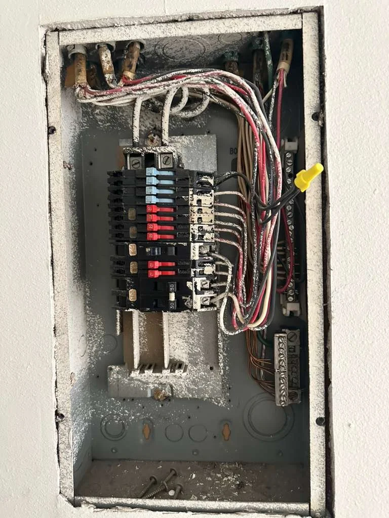 Open electrical breaker box with multiple wires, circuit breakers, and wiring components inside.