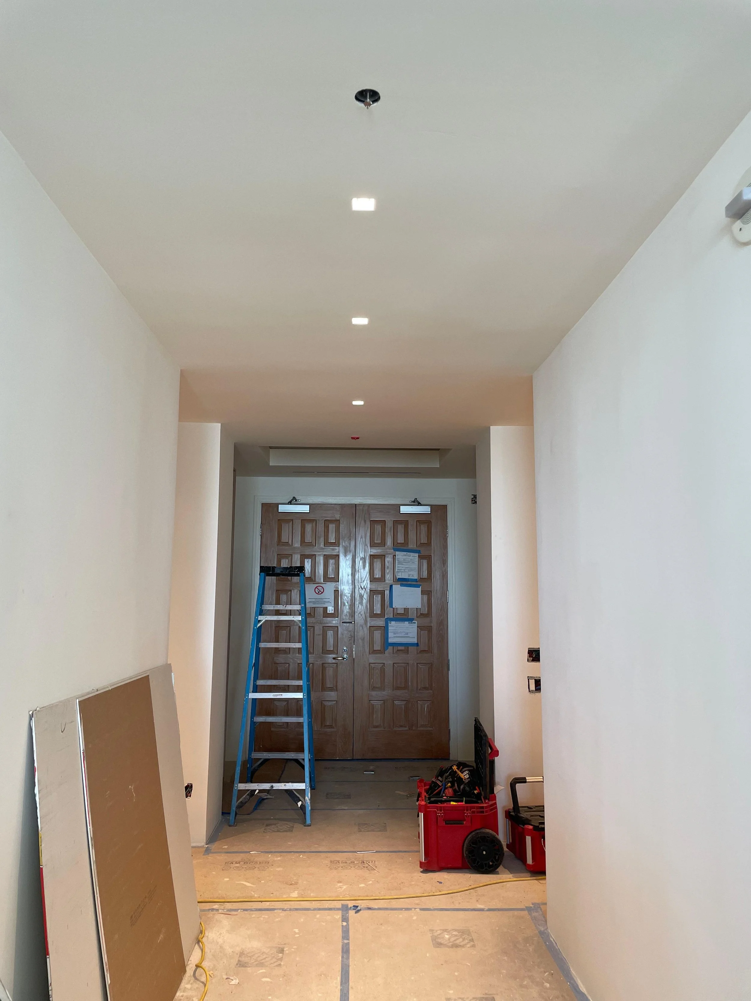 Interior hallway under construction with tools, a ladder, and construction materials.