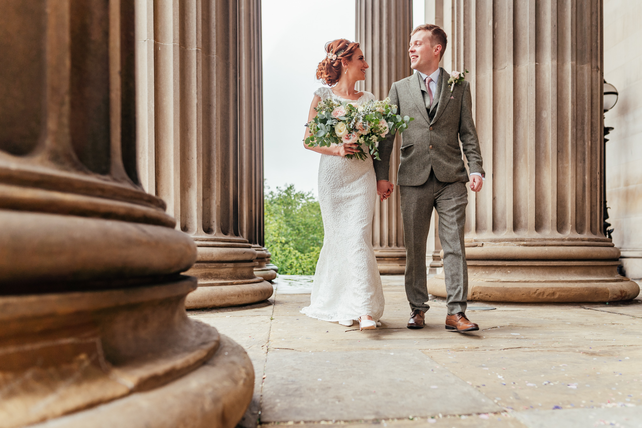Bride and Groom photograph walking hand in hand through the pillars outside St George’s Hall in Liverpool City Centre