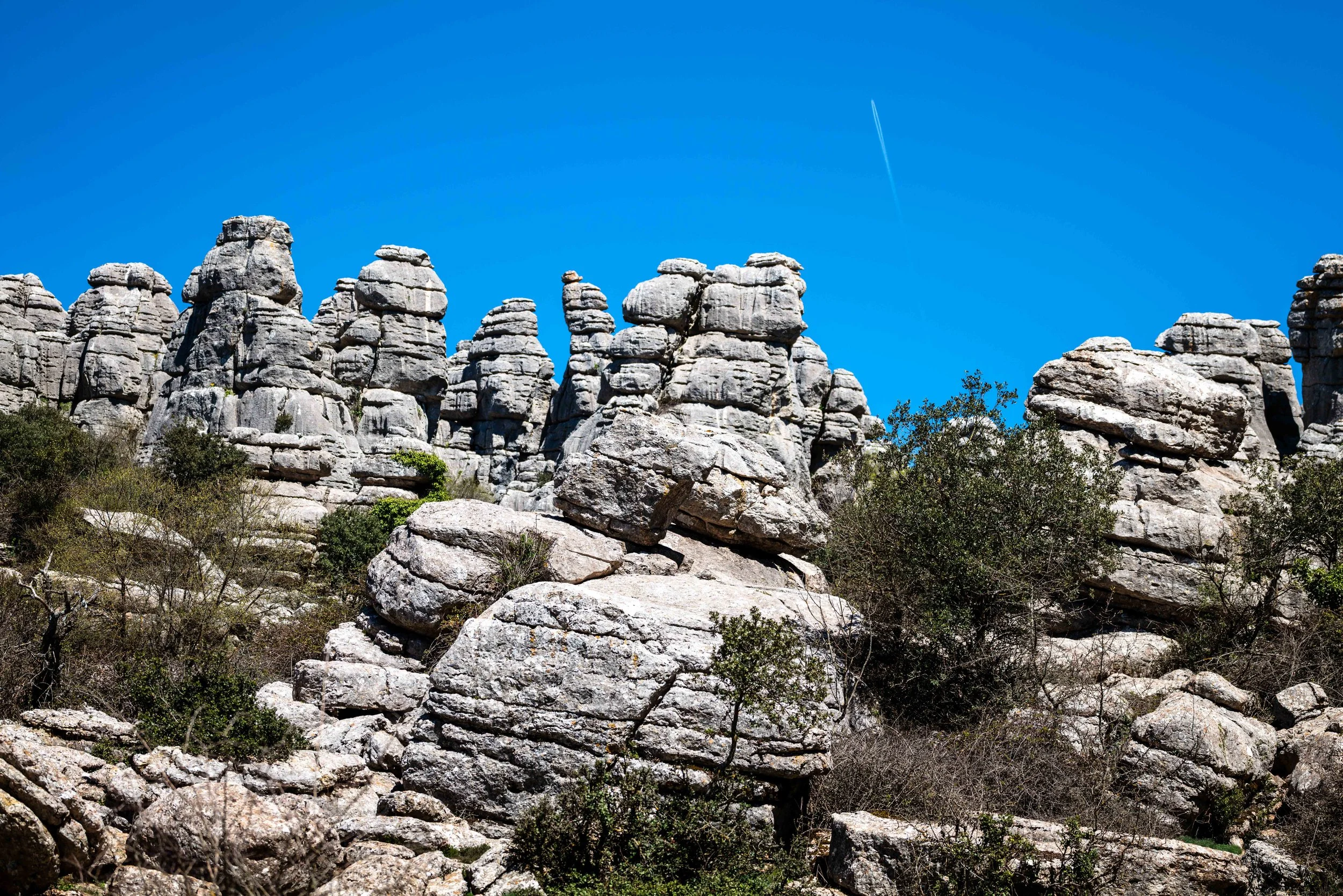Large gray rock formations and boulders under a clear blue sky with a faint contrail.