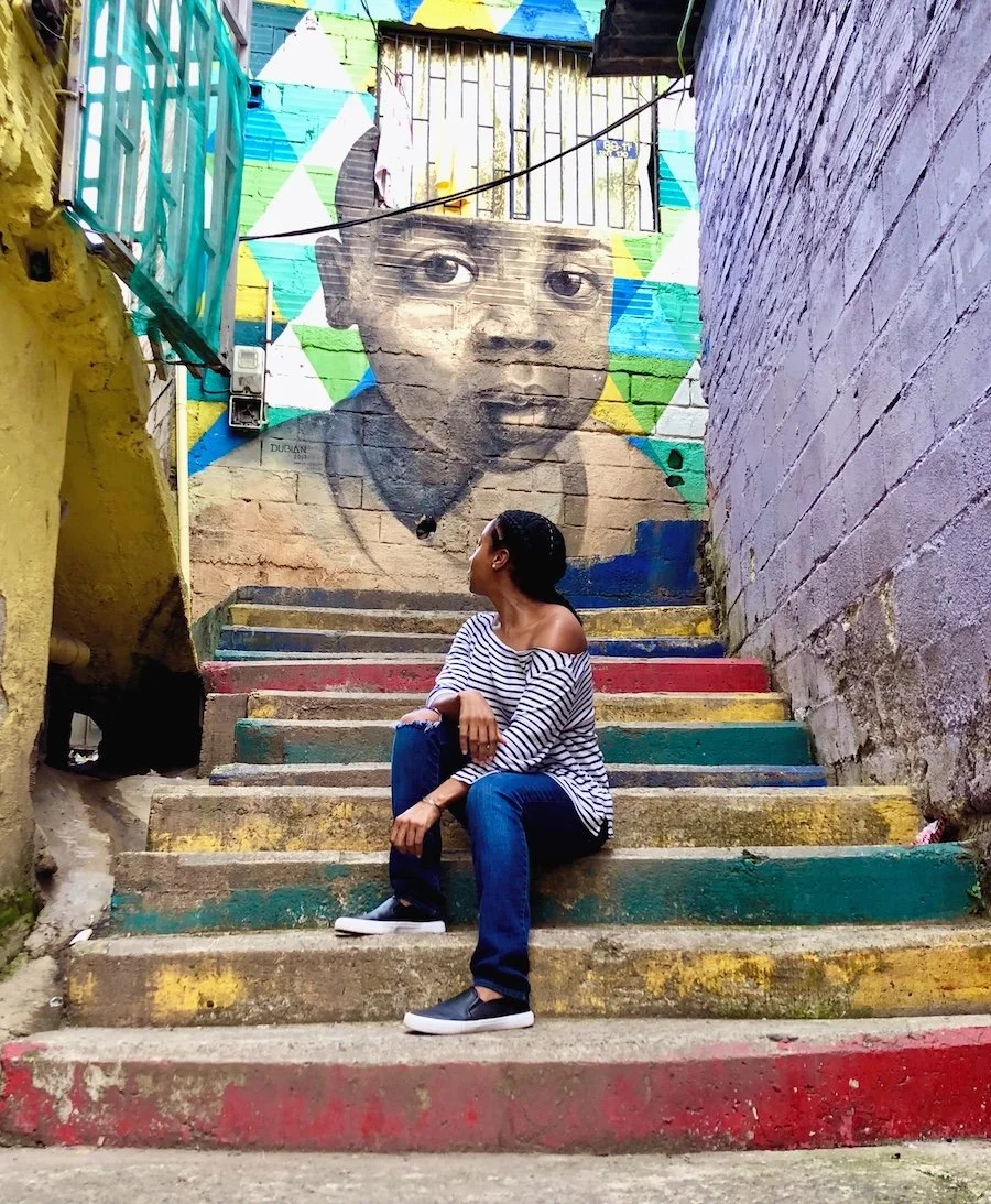 Leisan Echols sitting on colorful steps in front of a mural in Medellín, Colombia