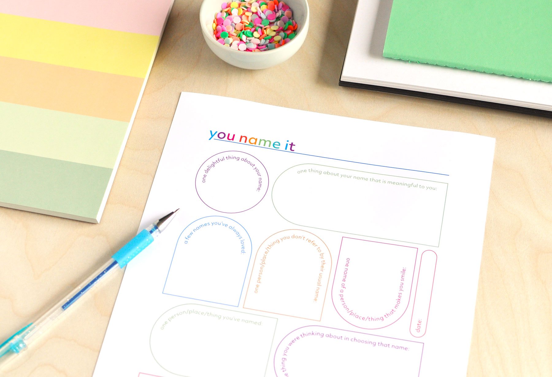 A colourful journal page titled You Name It, full of writing prompts about meaningful names in your life. Shown with blue pen and colourful notebooks.