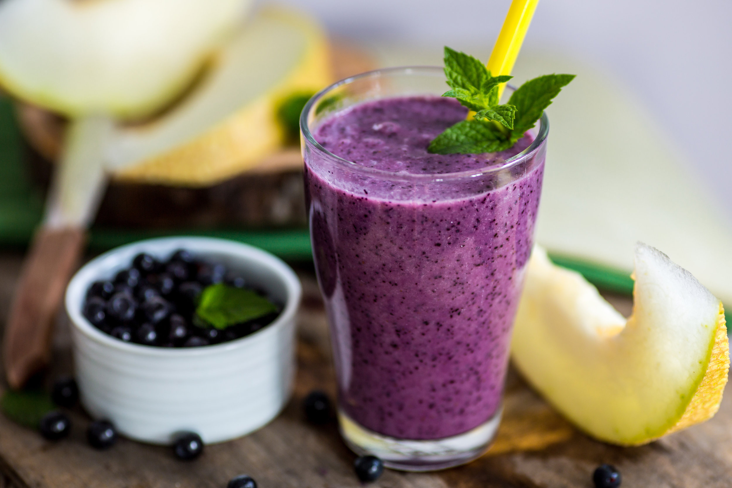 Blueberry smoothie in a glass with a straw and sprig of mint.jpeg