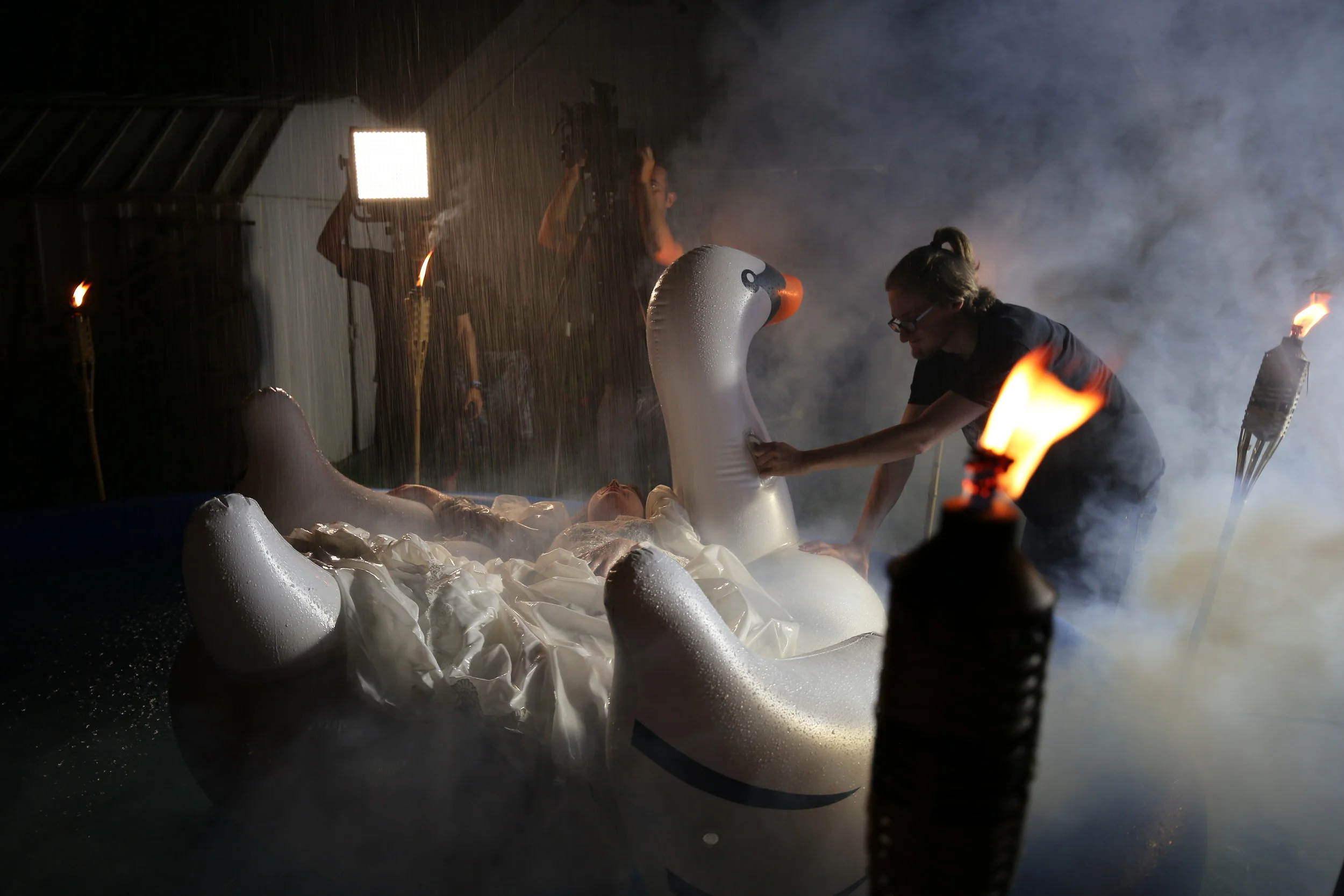 People working on a large white swan-shaped sculpture in a workshop with smoke and flames around.