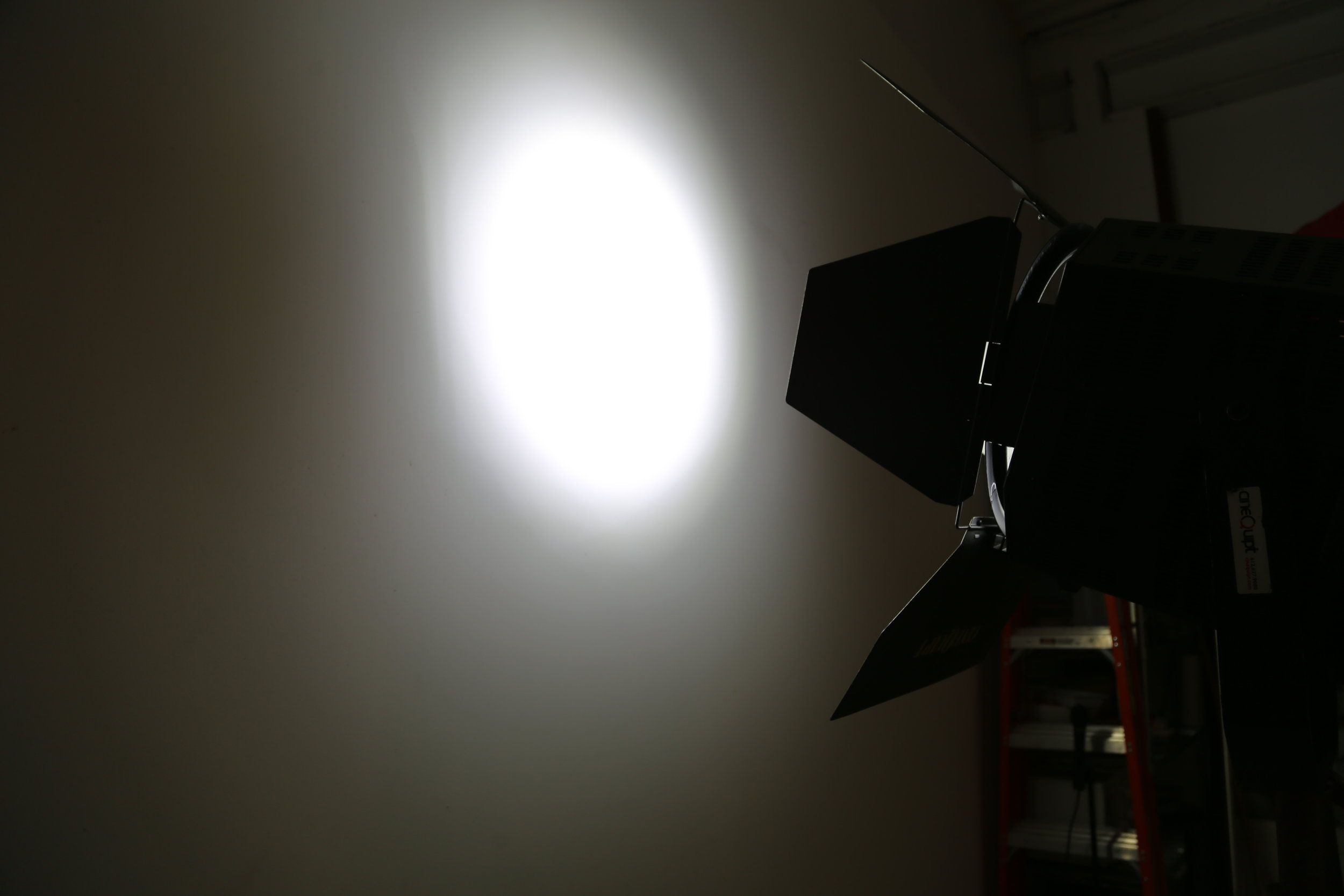 A projector casting light onto a blank wall in a dimly lit room, with shelves holding books in the background.