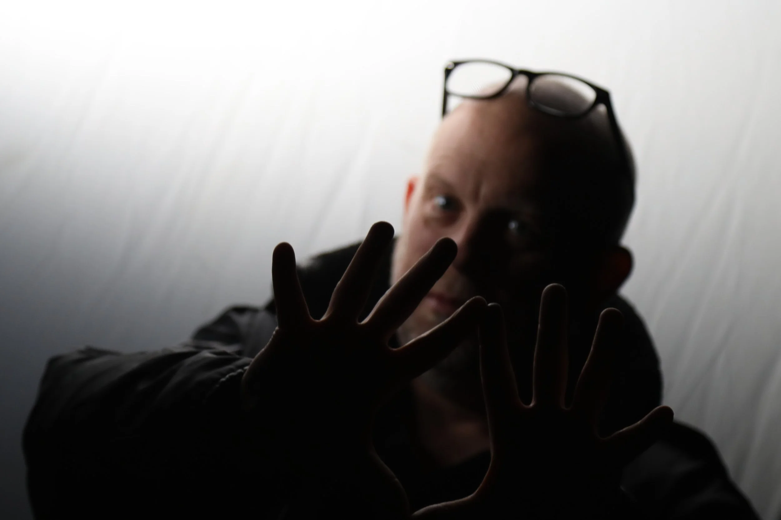 A person with glasses resting on their head, making a peace sign with two fingers, against a plain light background.