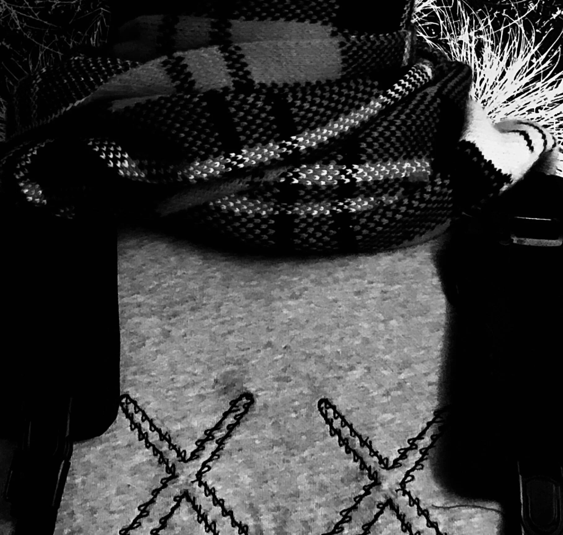 Black and white photo of a checkered patterned blanket draped over a chair, with a plush cat toy and chains on the floor.