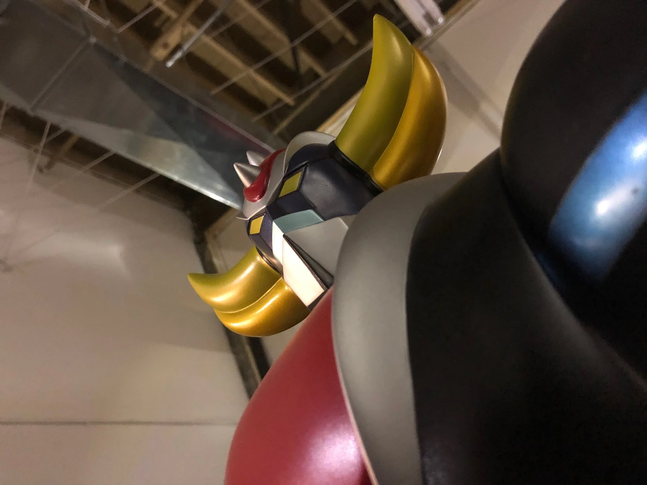 Close-up of a robot figure with a yellow and black arm, and a red and silver section, against a background of a metallic surface and wooden framing.