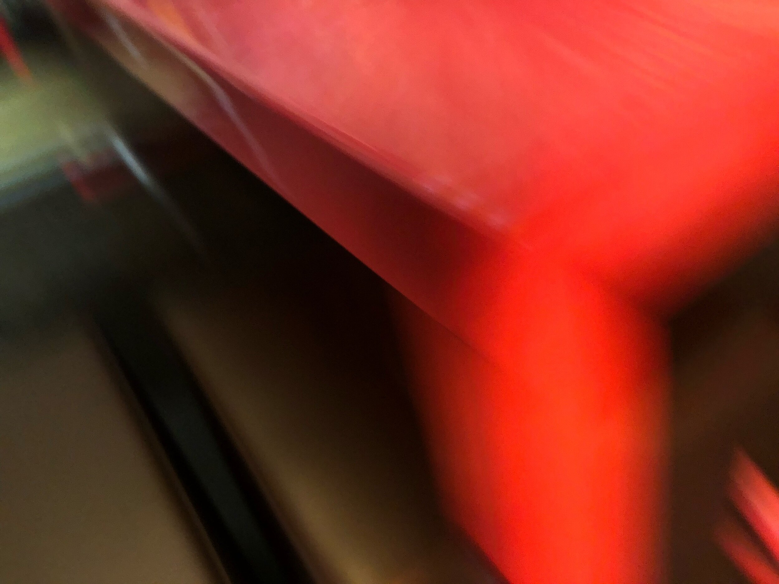 Close-up of a red, shiny surface, possibly a car or electronic device, with a black edge or frame in the lower left corner.