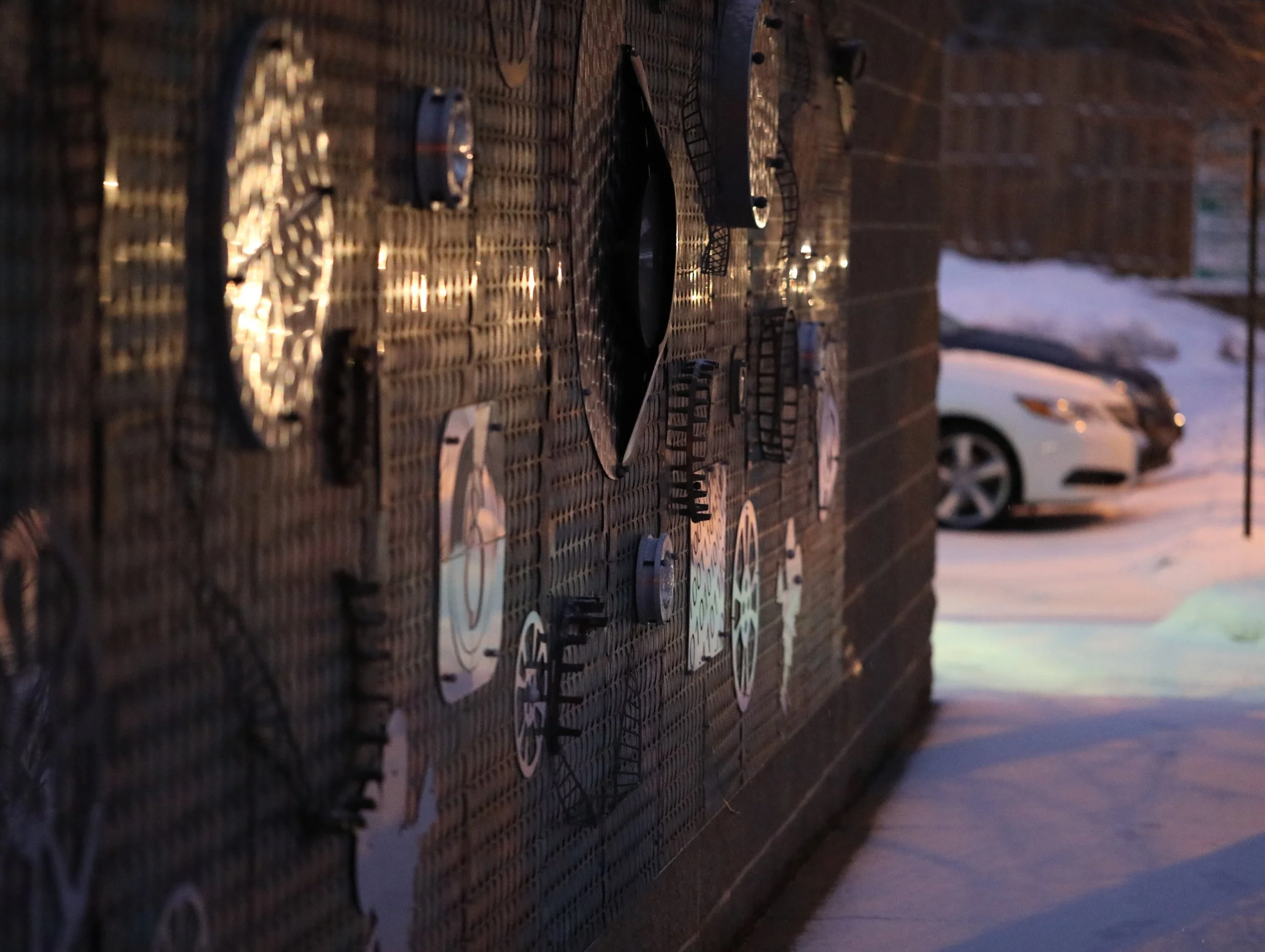 Close-up of a stacked pile of black plastic trays or pallets with several white paper labels attached, in an outdoor setting with snow and parked cars in the background.