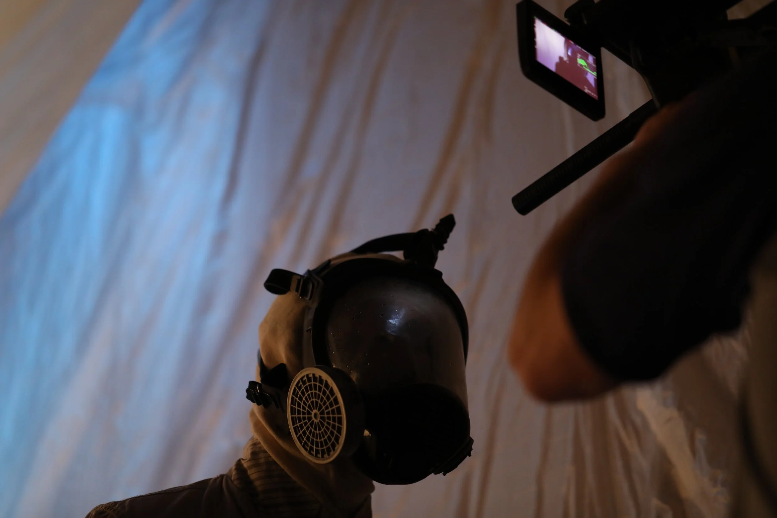 A person operating a camera on a tripod, recording or taking photos in a room with wooden flooring.