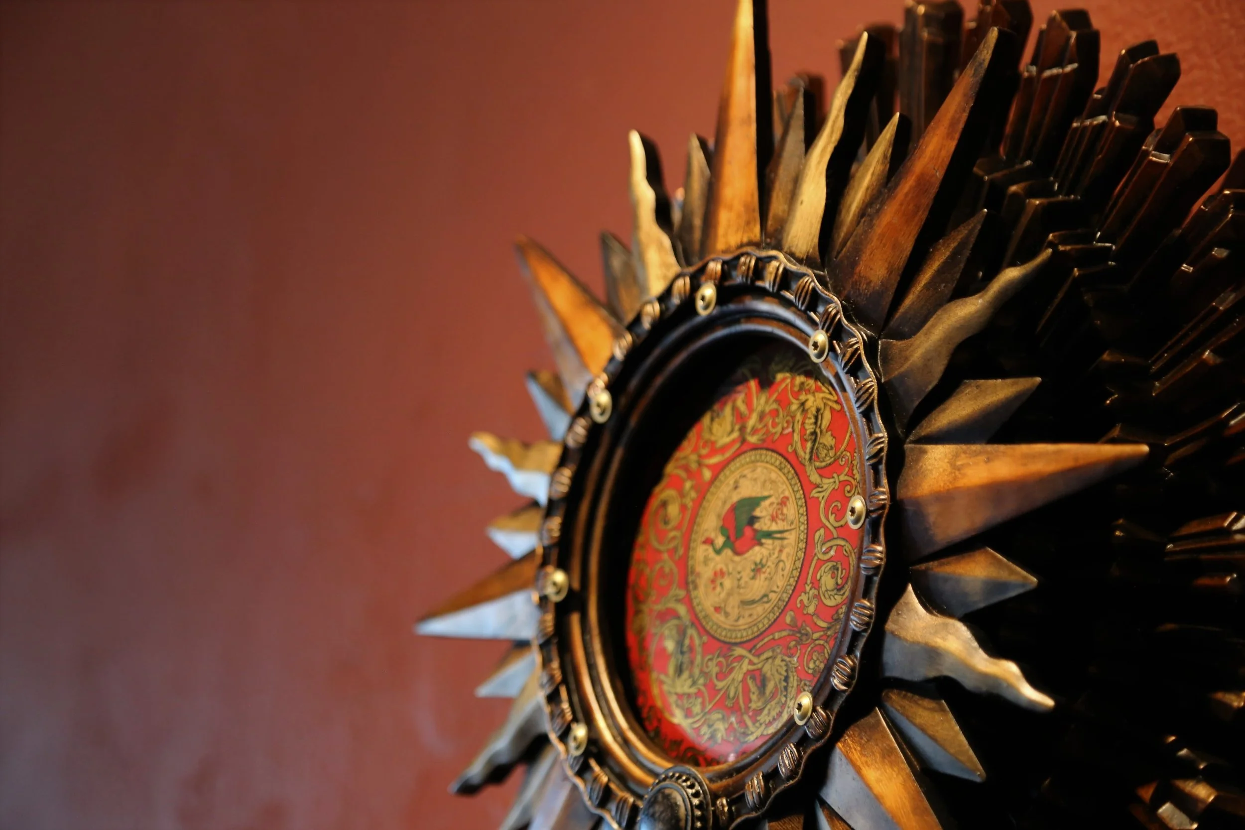 Close-up of a decorative round wall mirror with a sunburst metal frame and a heraldic emblem in the center.