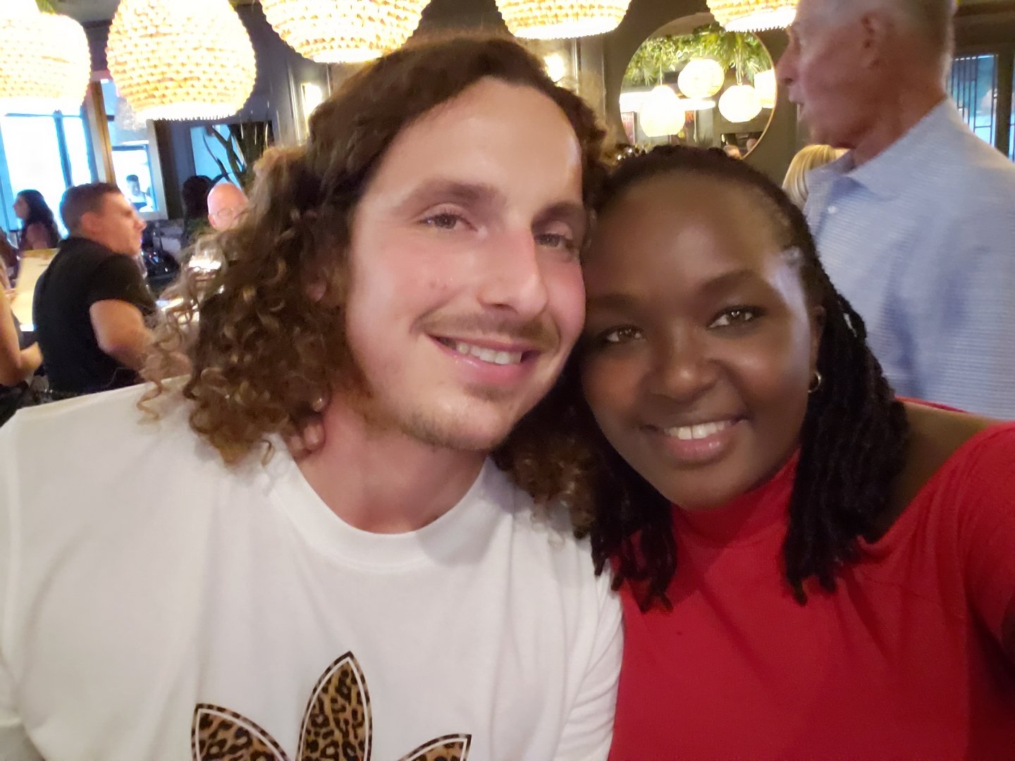 Two people smiling in a warmly lit restaurant with decorative hanging lights.