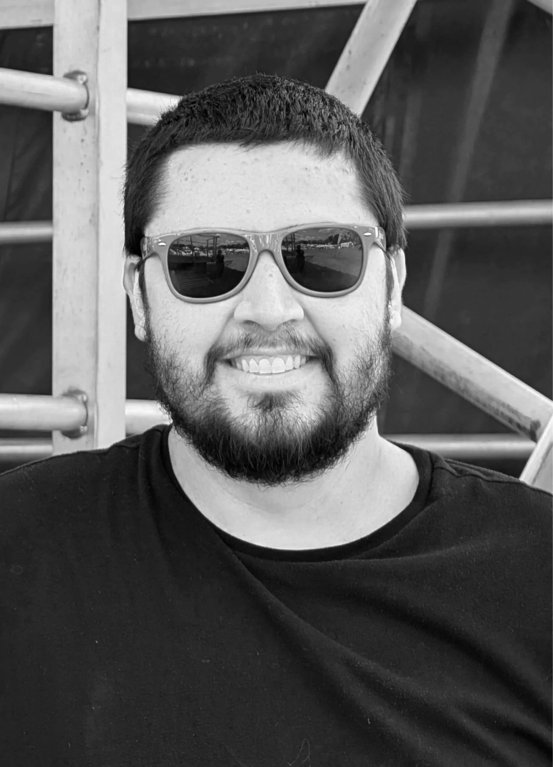 Man wearing green sunglasses and a black shirt, smiling outdoors.