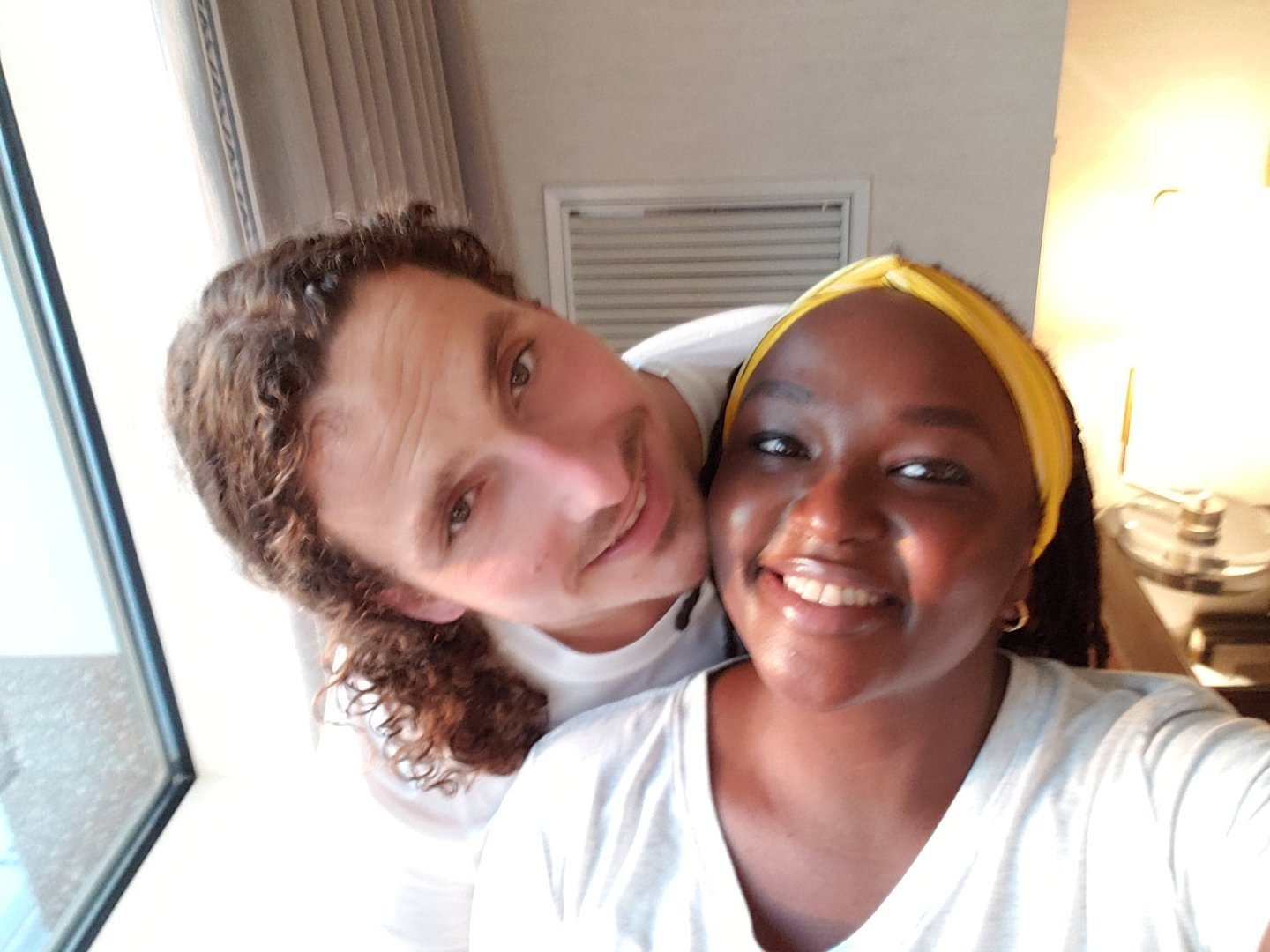 A smiling couple taking a selfie near a window.