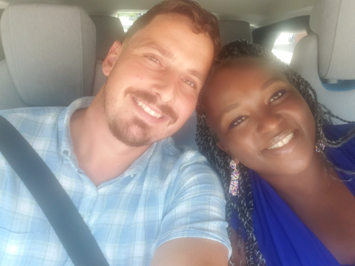 Two people seated in a car, smiling and posing for a selfie.